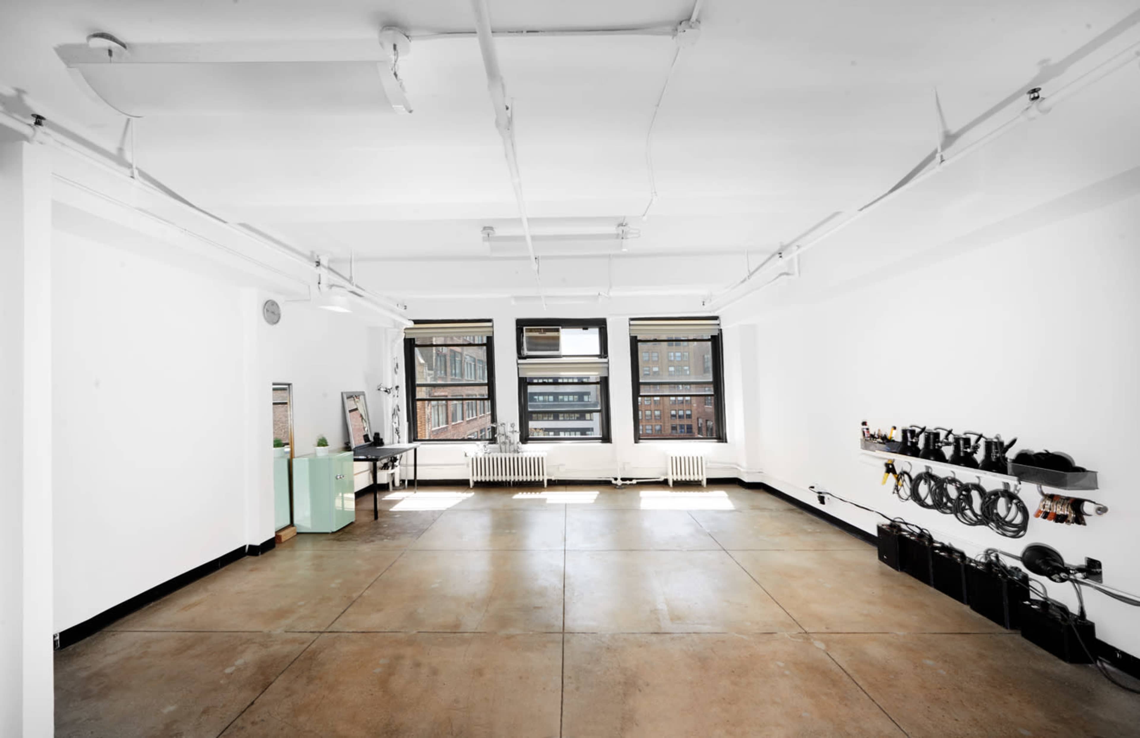 A spacious, empty room with concrete flooring, large windows, and equipment mounted on the wall.