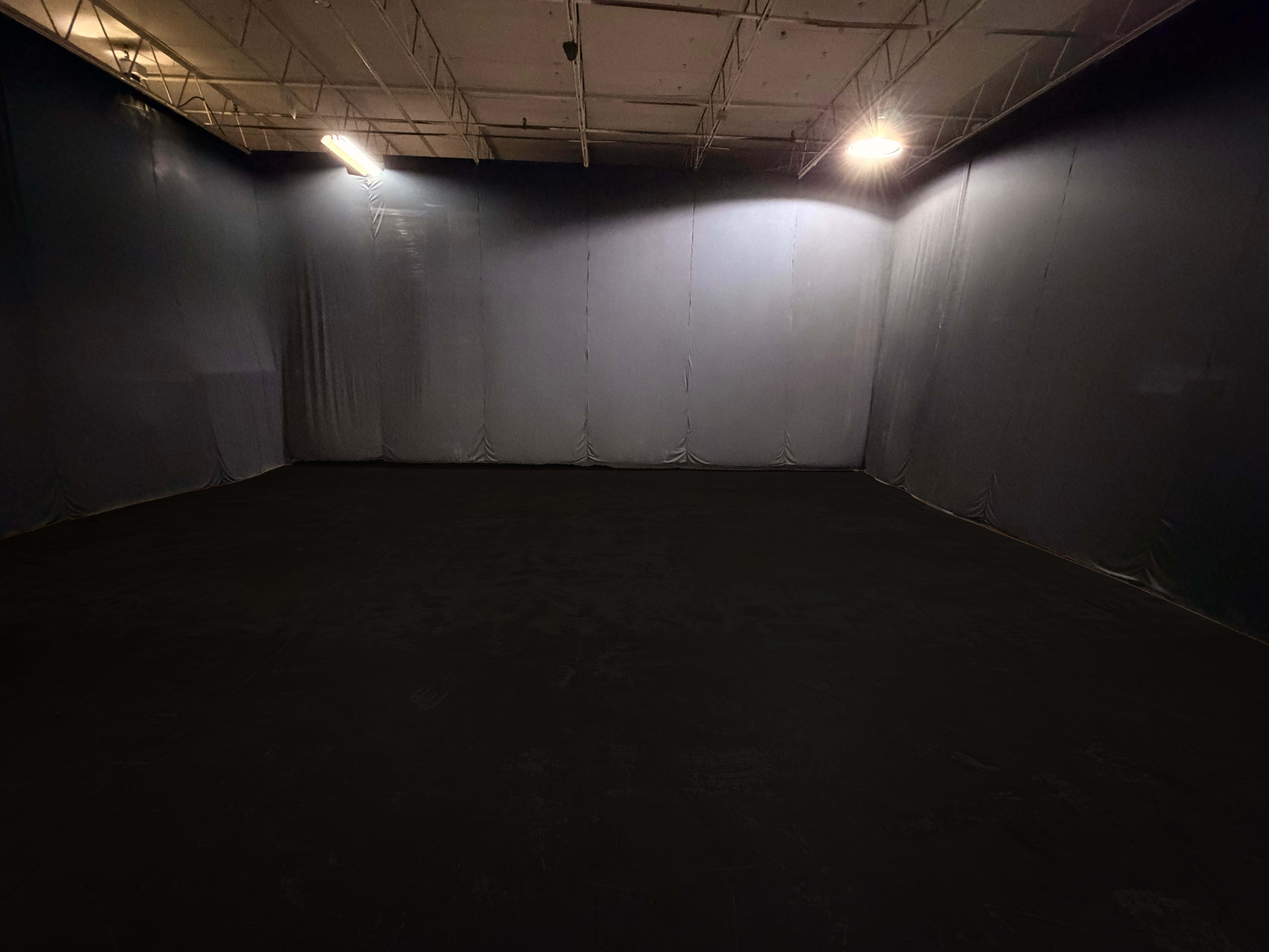 The image shows a dimly lit room with gray walls and a black floor, featuring an empty space devoid of furniture or objects.