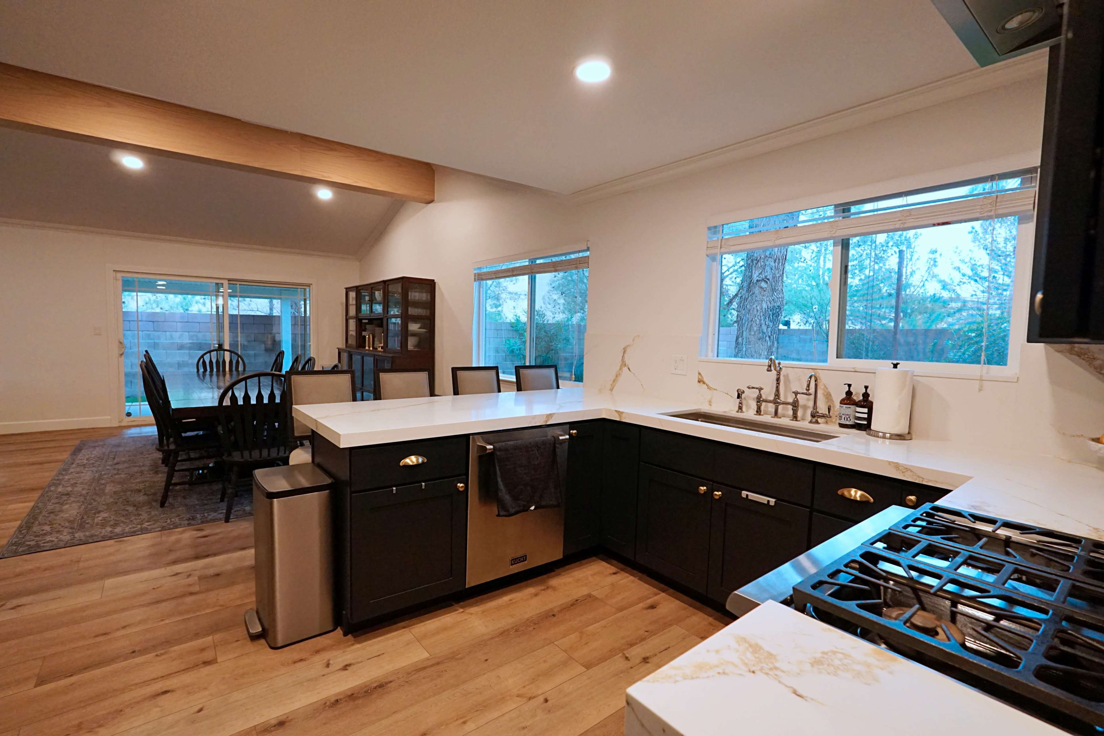 A modern kitchen features dark cabinets, a white countertop, and a stove near a large window overlooking an outdoor space.