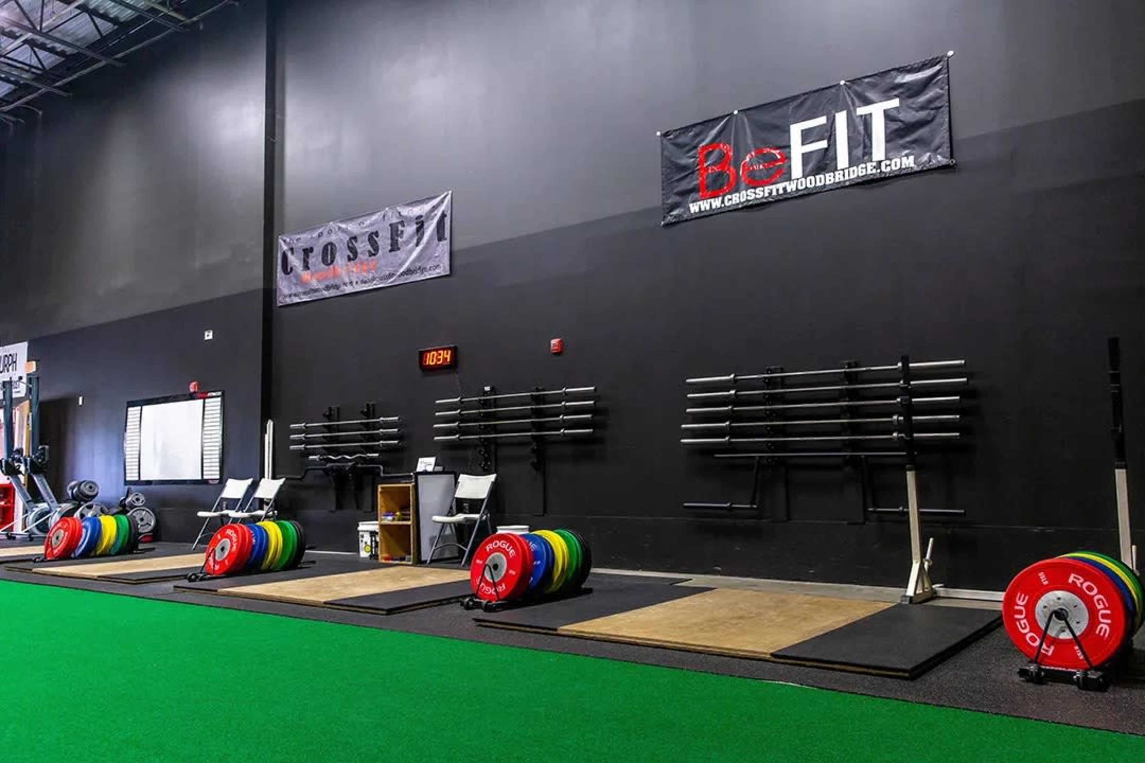 A weightlifting area with colorful bumper plates on the floor, multiple lifting platforms, and a black wall displaying banners for CrossFit and BeFIT.