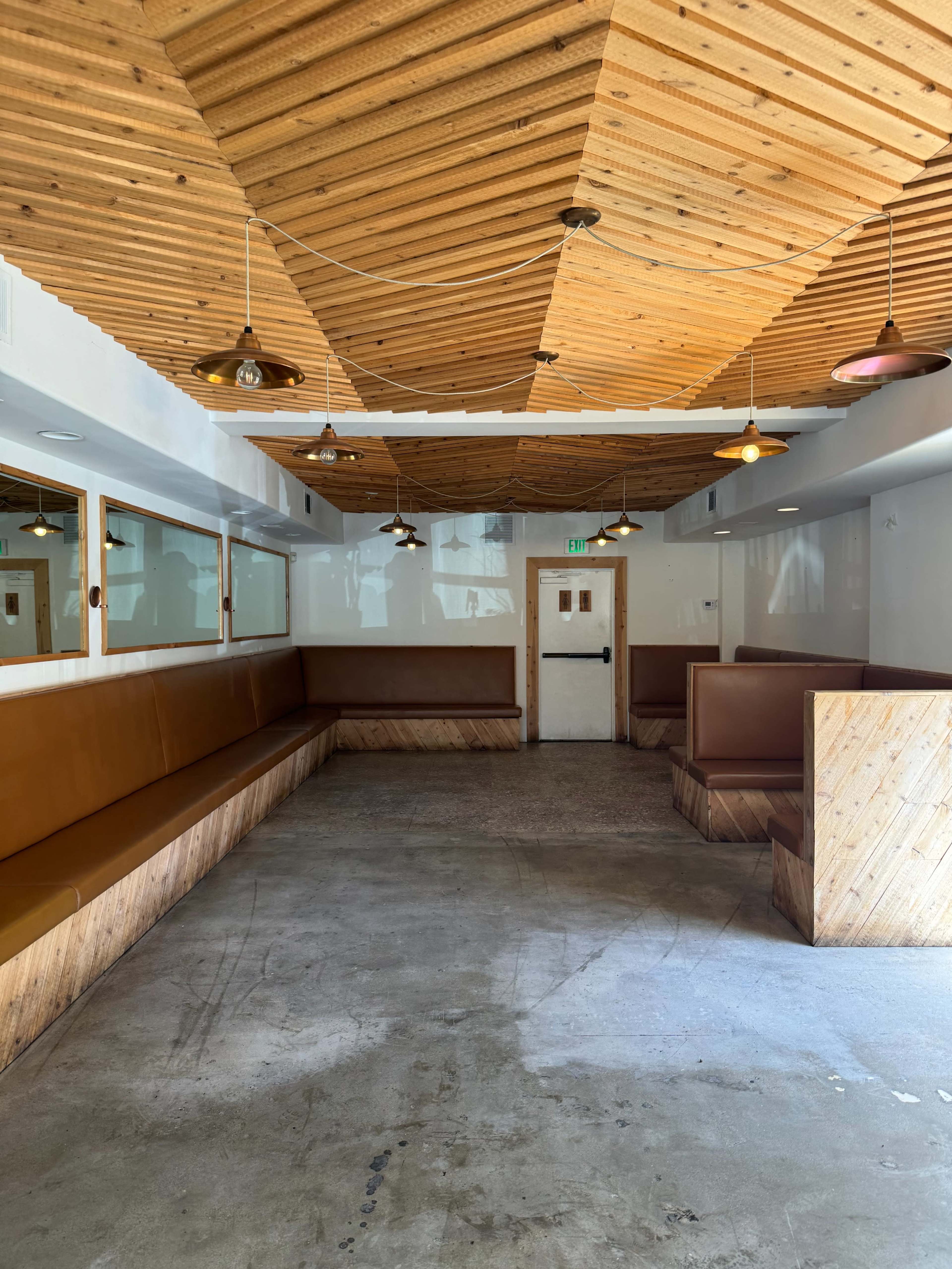 The interior features wooden paneling on the ceiling and brown upholstered benches along the walls in a spacious, empty restaurant setting.