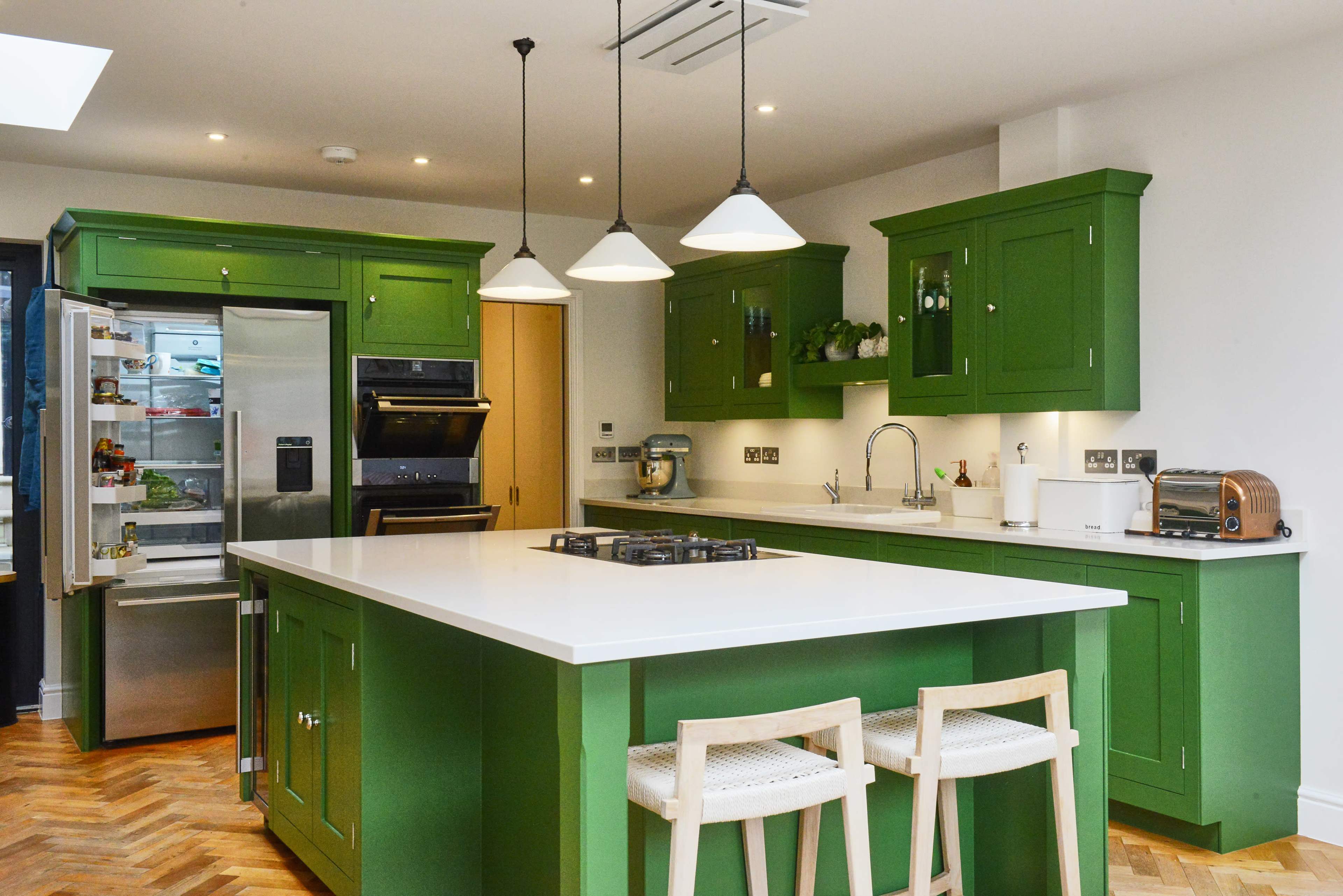 The kitchen features green cabinetry, a central island with a stovetop, and modern appliances, creating a functional cooking space.