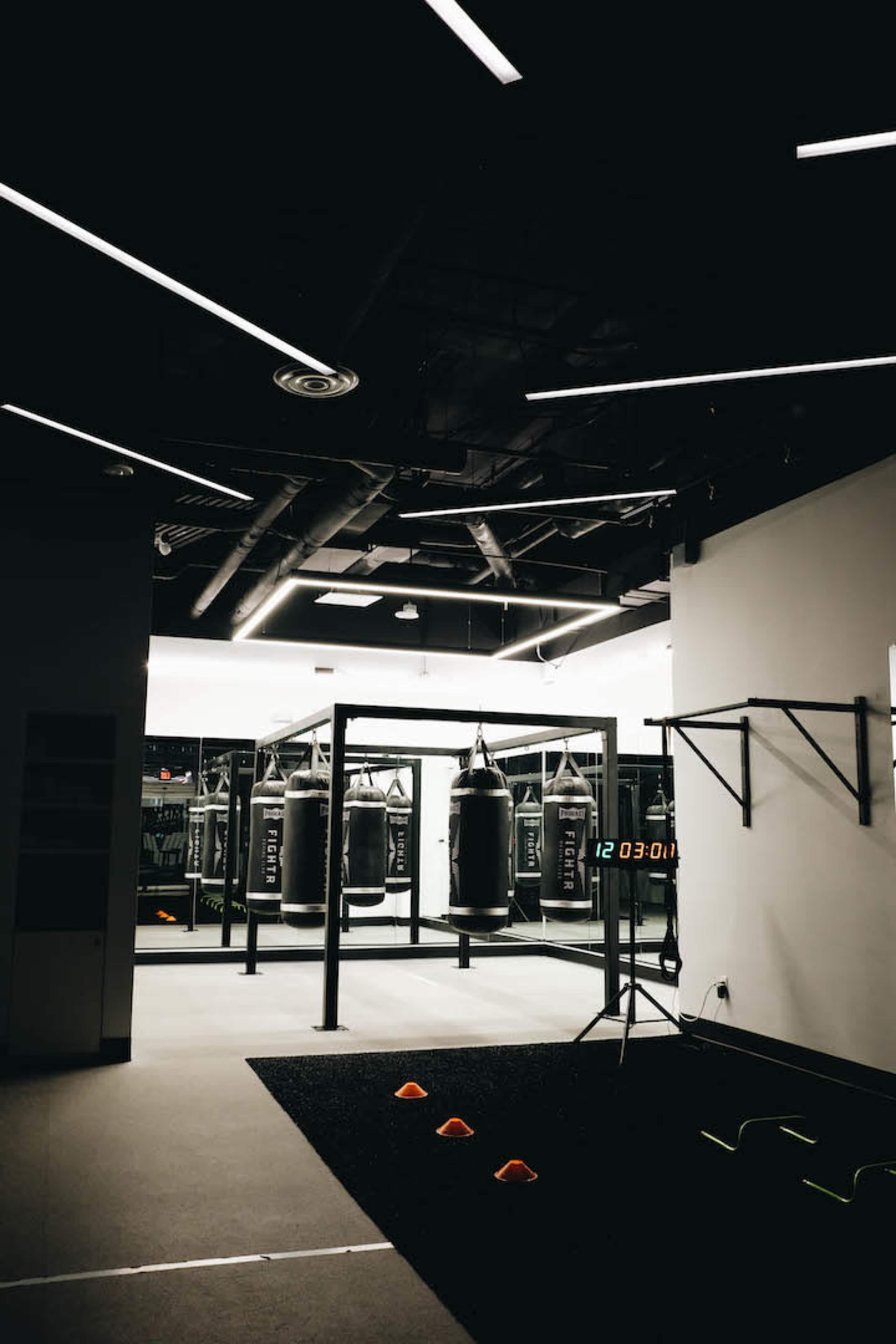 A dimly lit gym featuring several punching bags, a countdown timer, and training equipment.