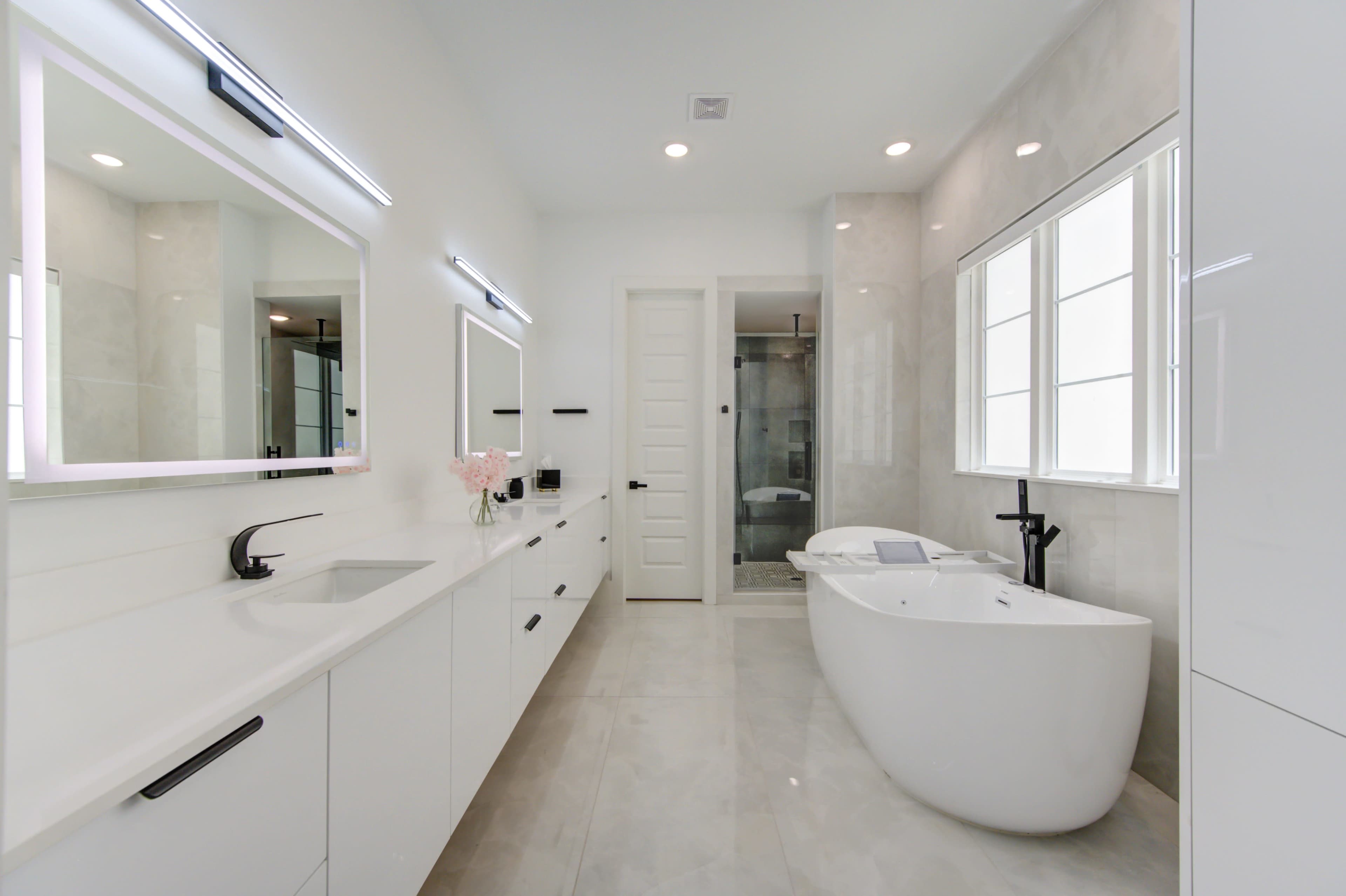 A modern bathroom featuring a freestanding bathtub, a double vanity with illuminated mirrors, and a glass-enclosed shower.