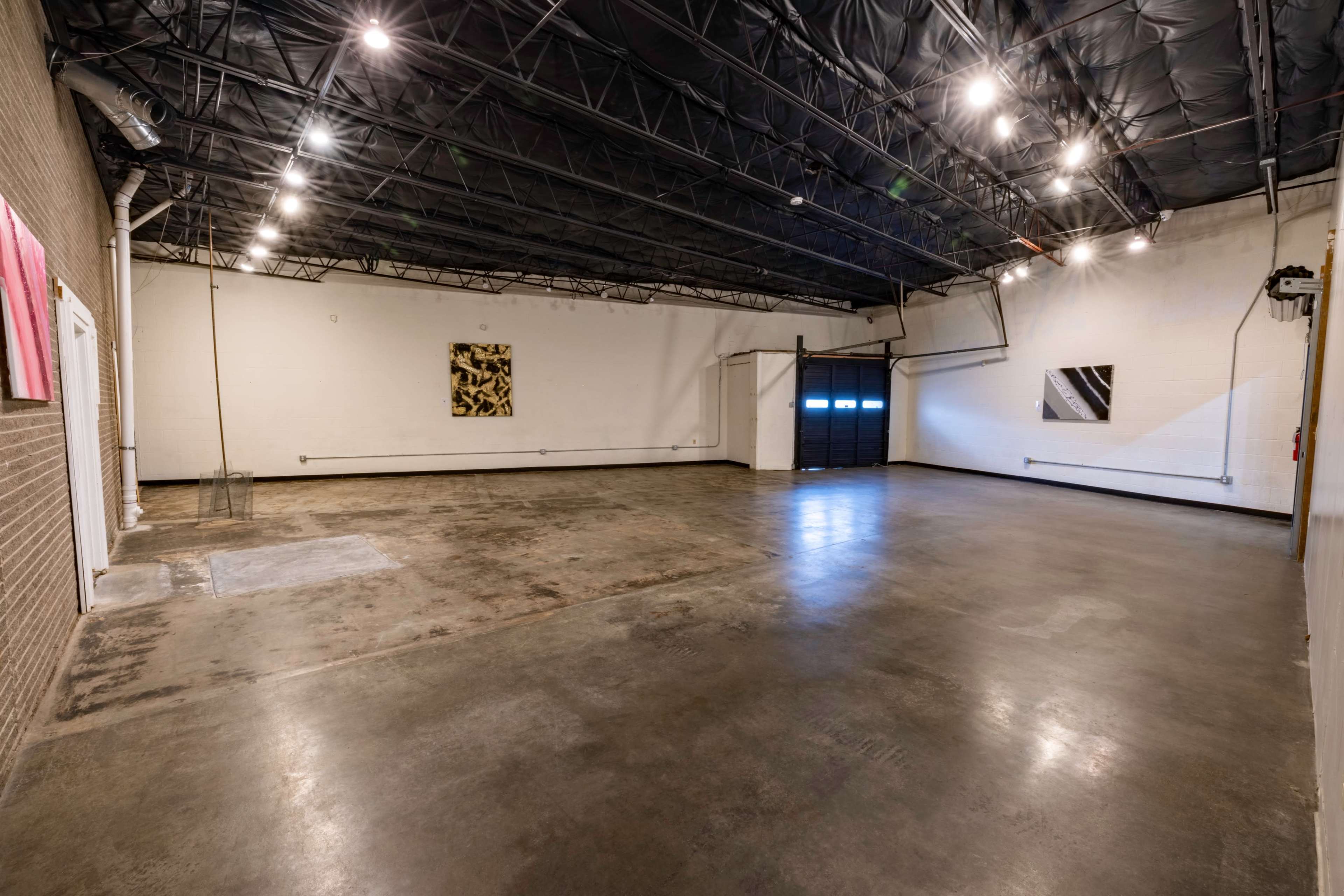 An empty industrial space with a polished concrete floor, dim lighting, and two abstract art pieces on the walls.