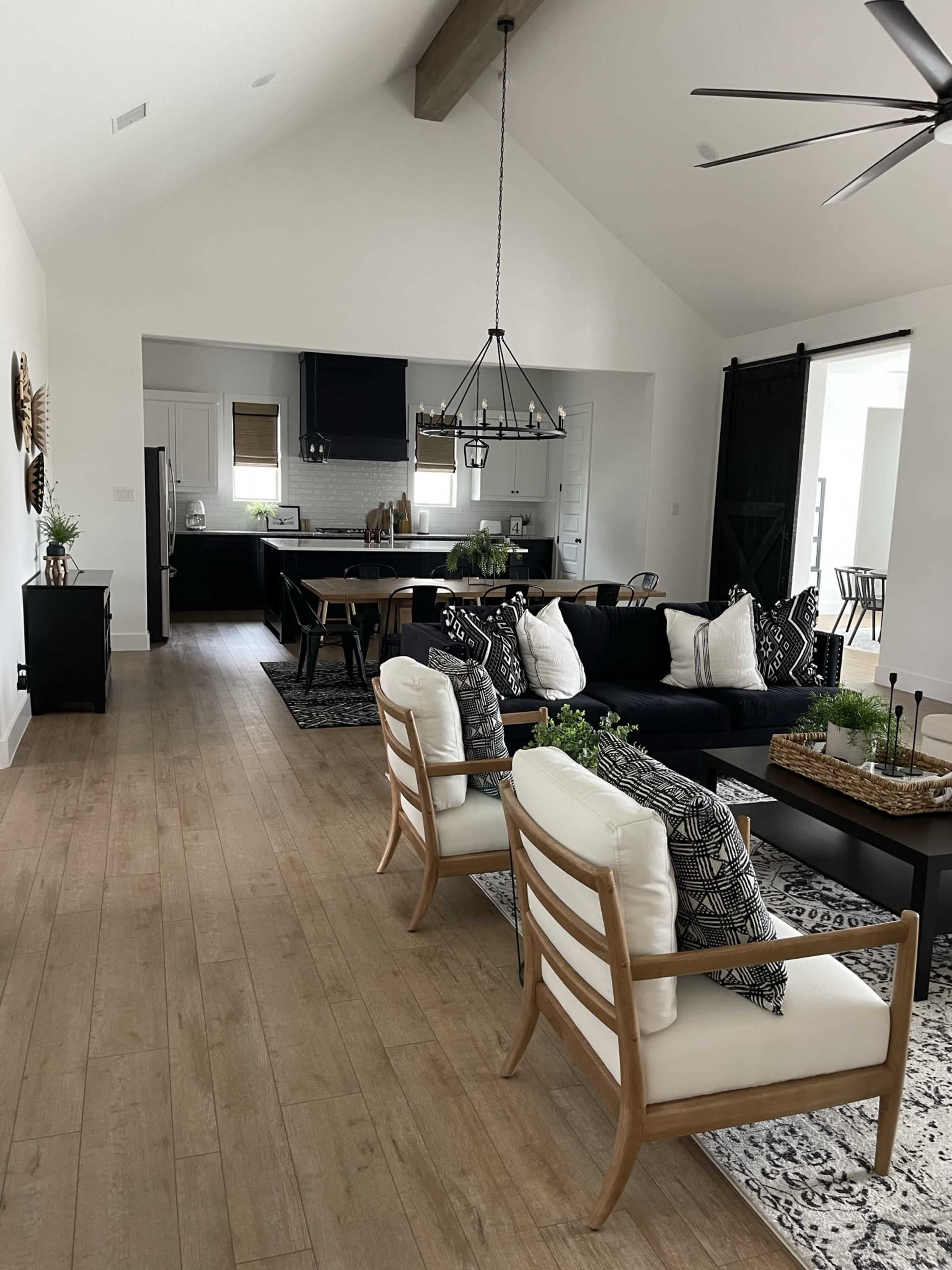 A modern open-concept living space with a black sofa, wooden dining table, and decorative plants.