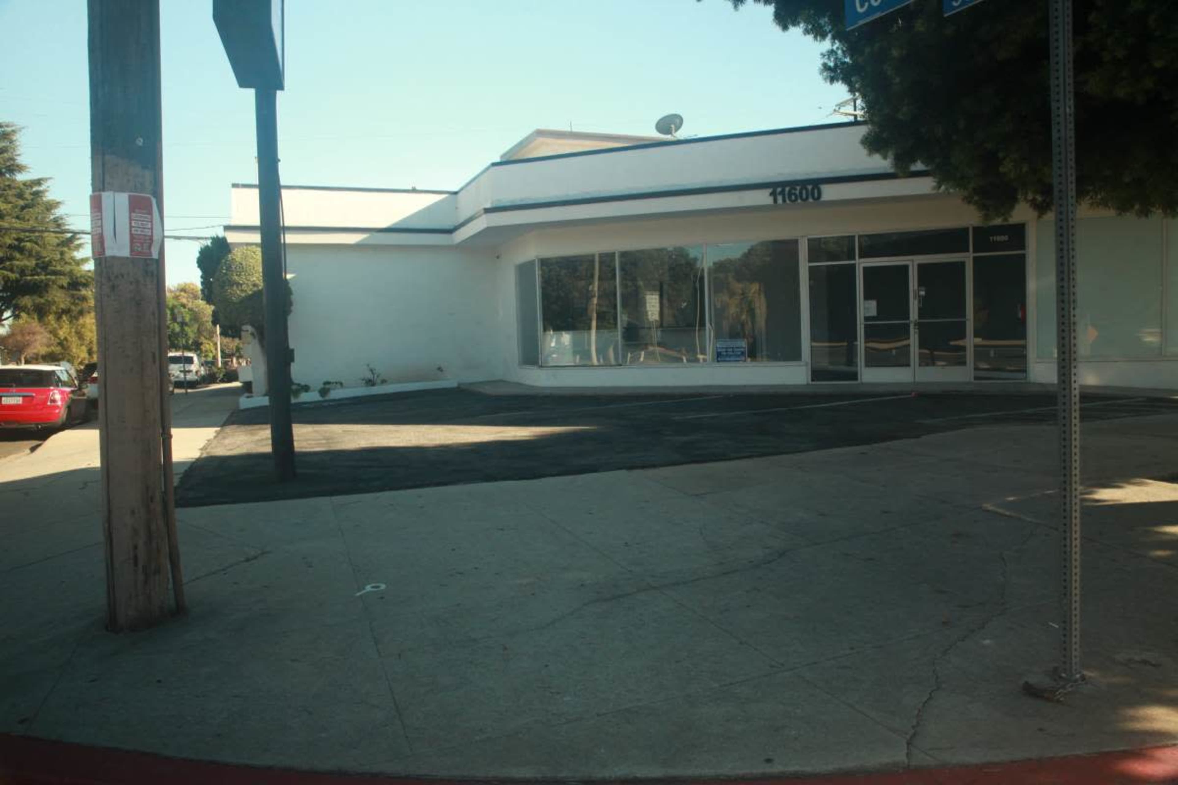The image shows a vacant commercial building at 11600, with a paved parking area and a street sign nearby.