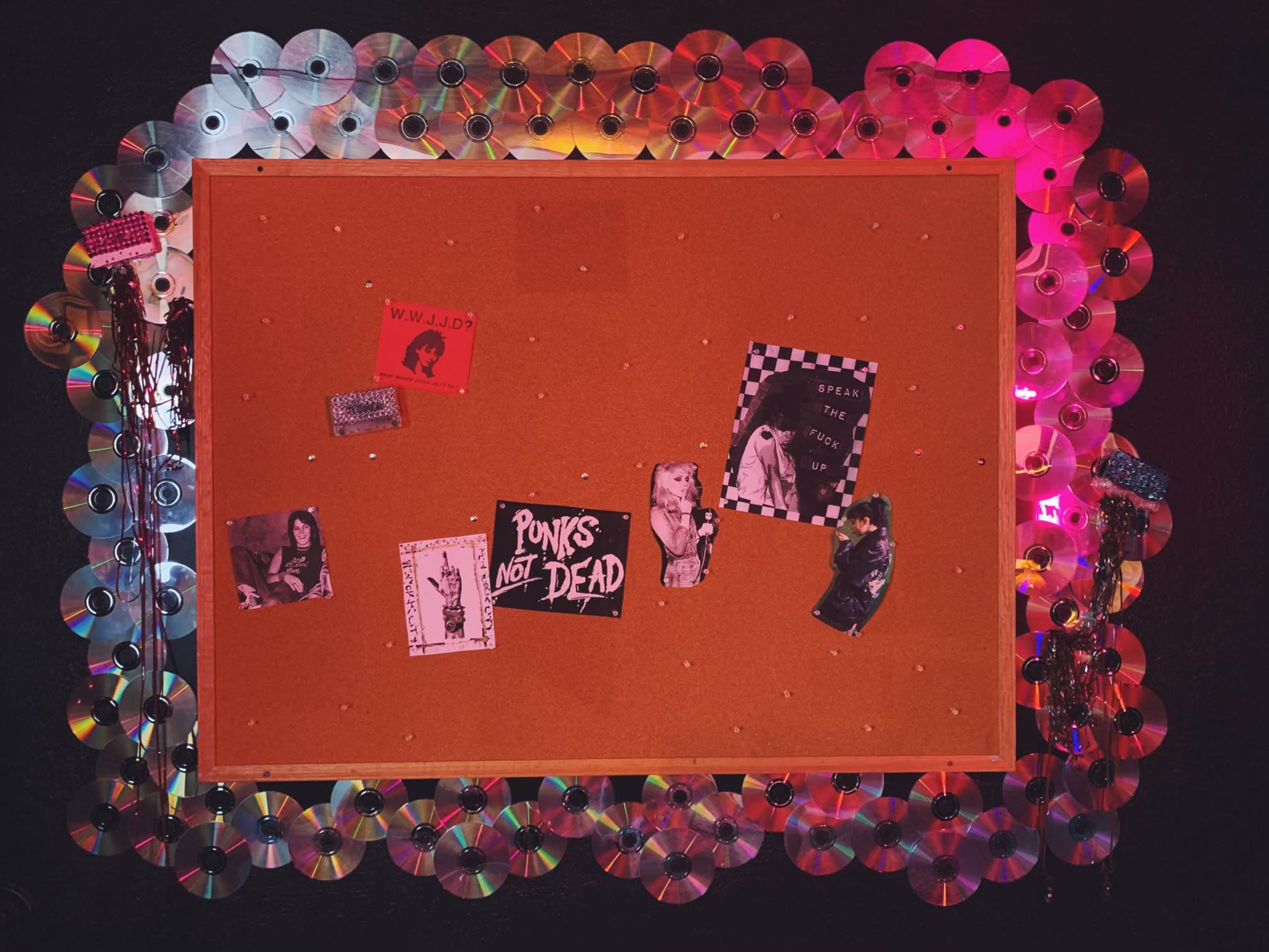 A corkboard surrounded by colorful CDs displays various posters and photographs related to punk culture.