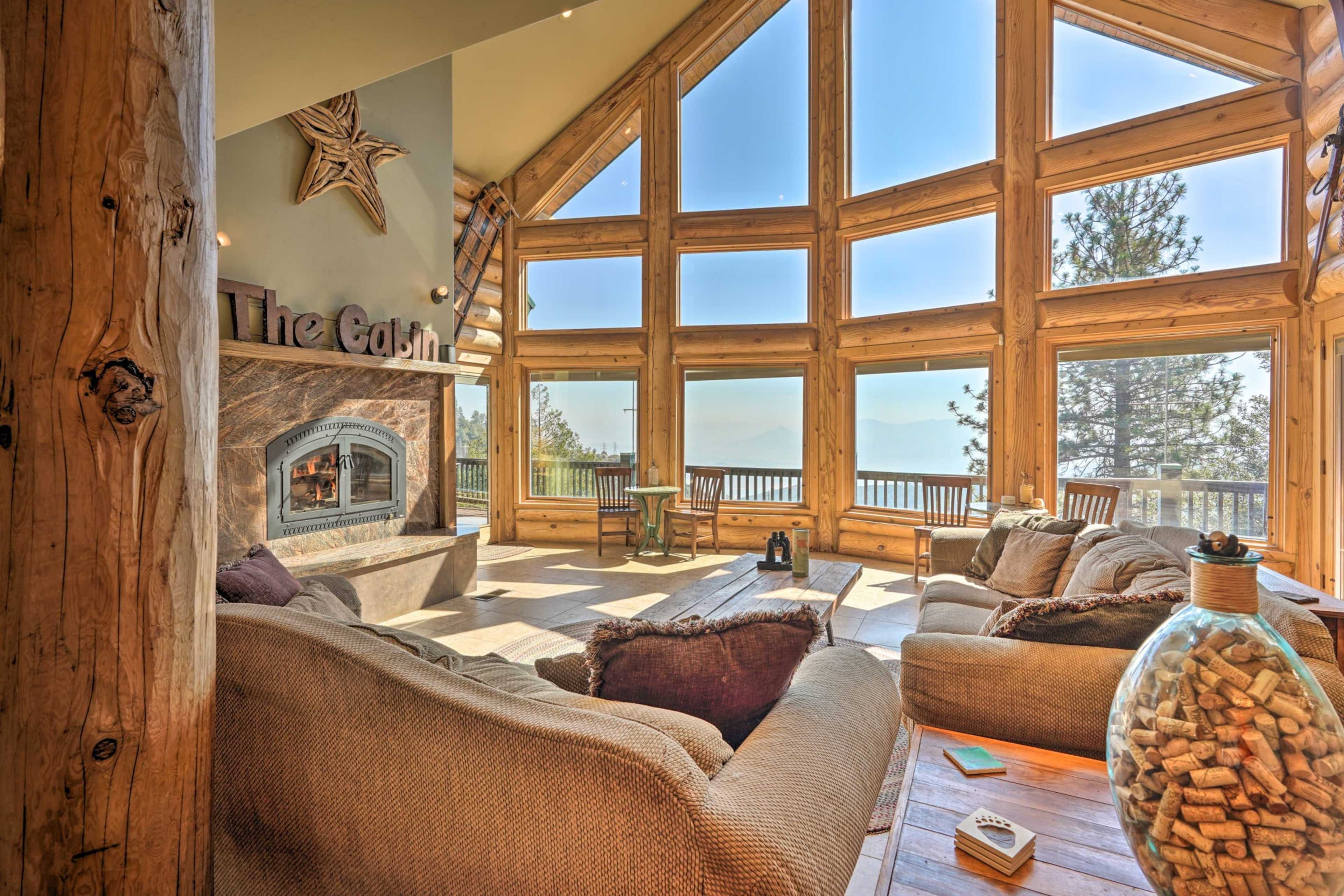 A spacious living room features large windows with mountain views, a stone fireplace, and cozy seating arrangements.