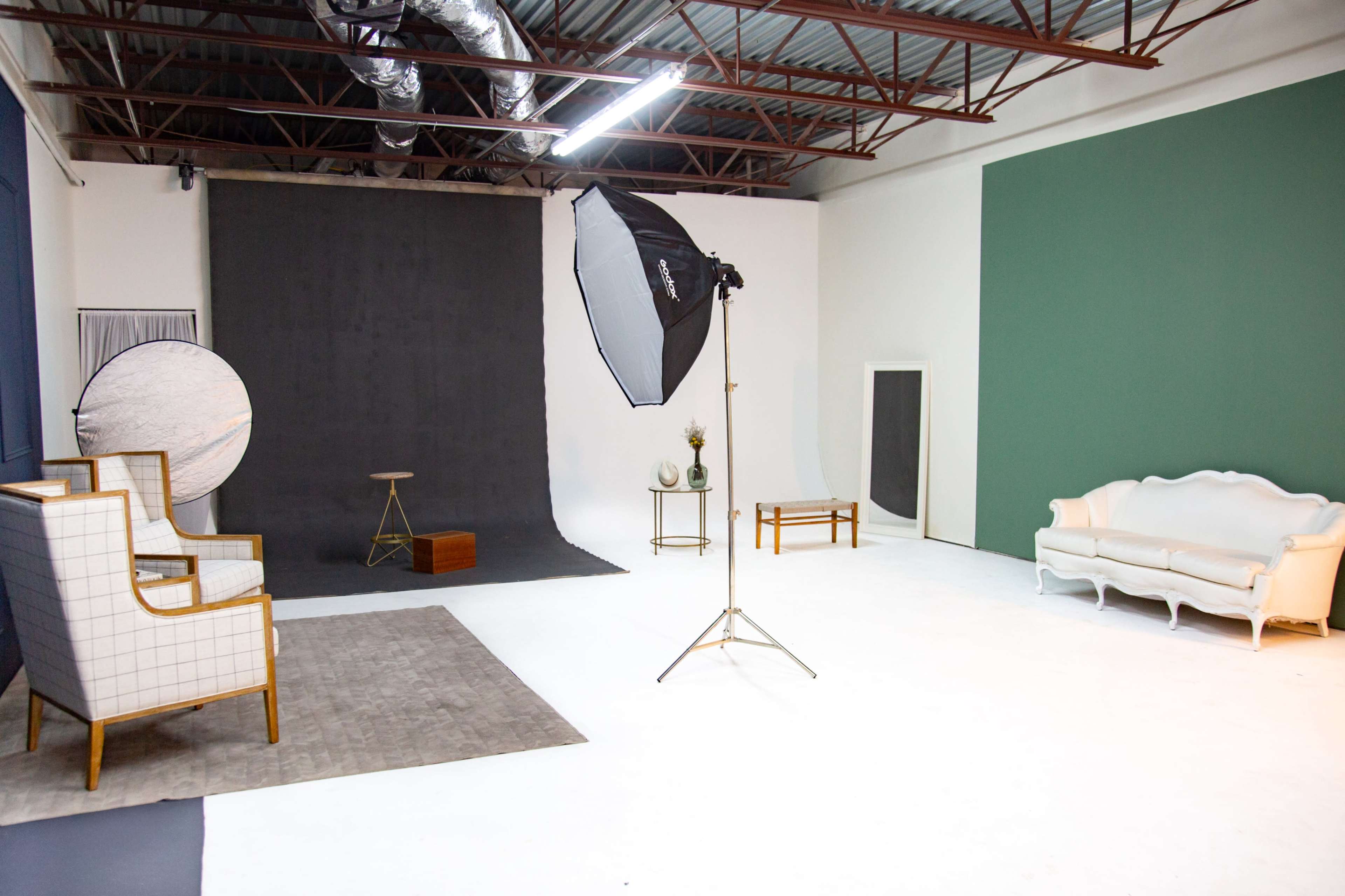 The image shows a photography studio with various props, including chairs, a table, and backdrops.