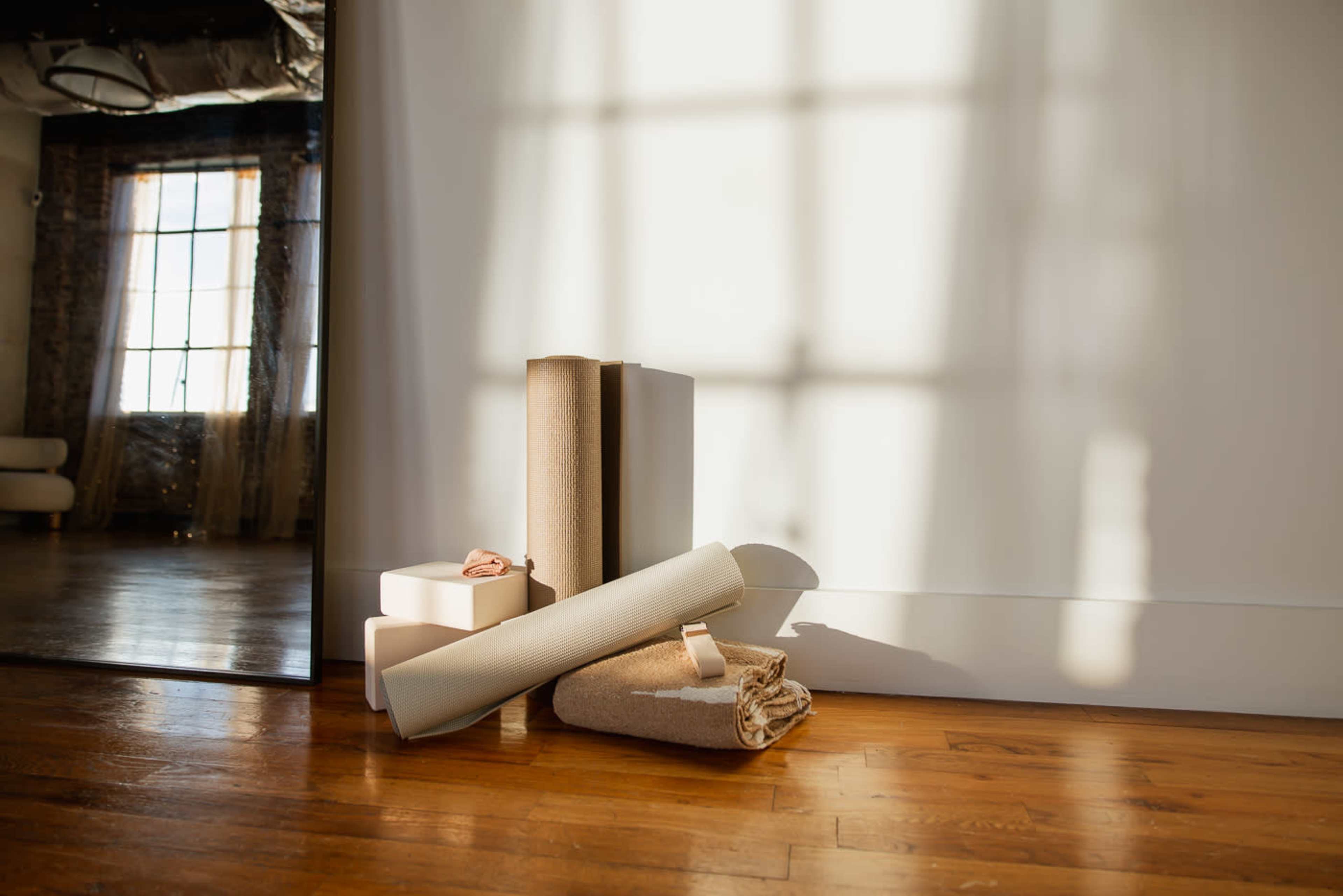The image shows rolled textiles and a stack of boxes resting against a wall in a well-lit room with wooden flooring.