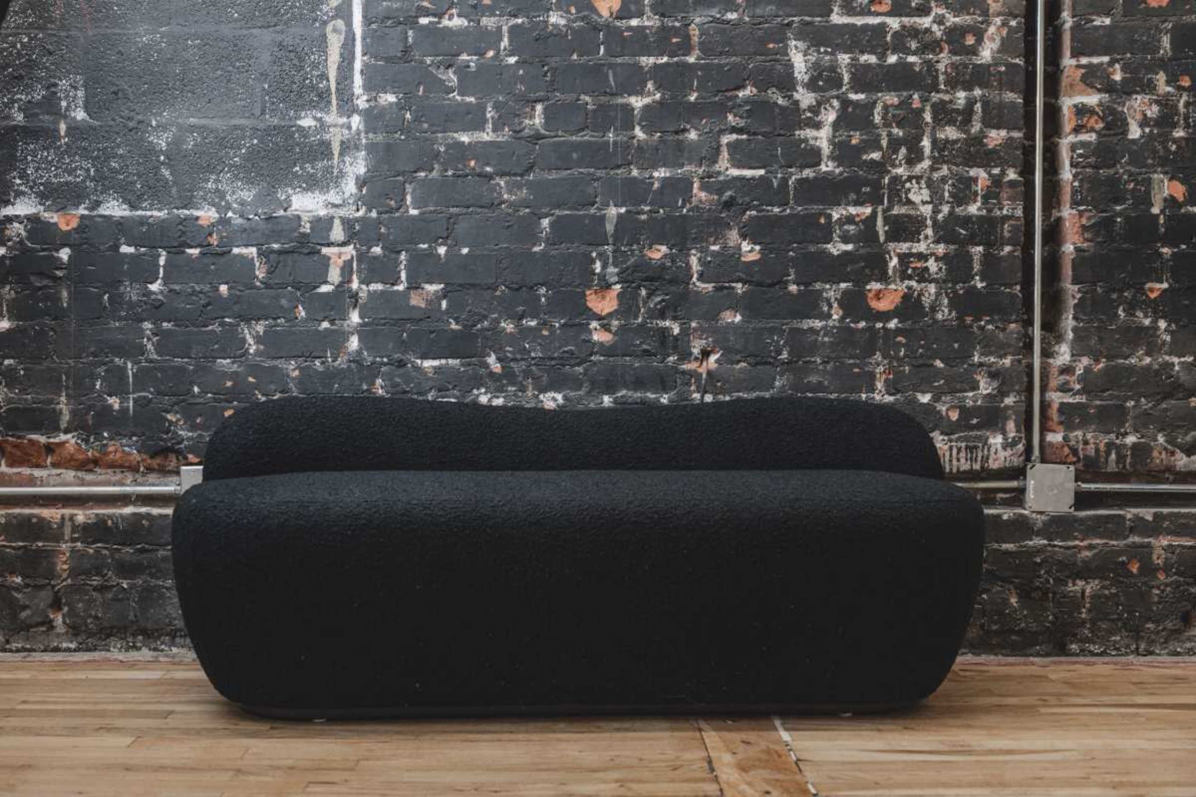 A black, curved sofa is positioned against a distressed brick wall with visible peeling paint.