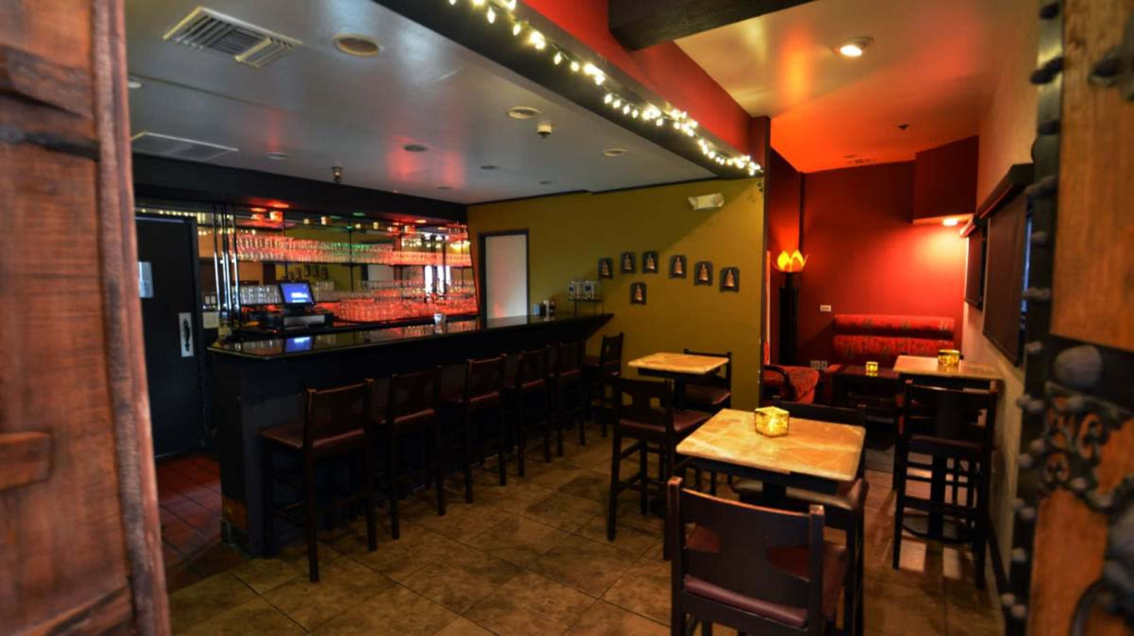 A dimly lit bar area with a long counter, wooden tables, and framed pictures on the walls.