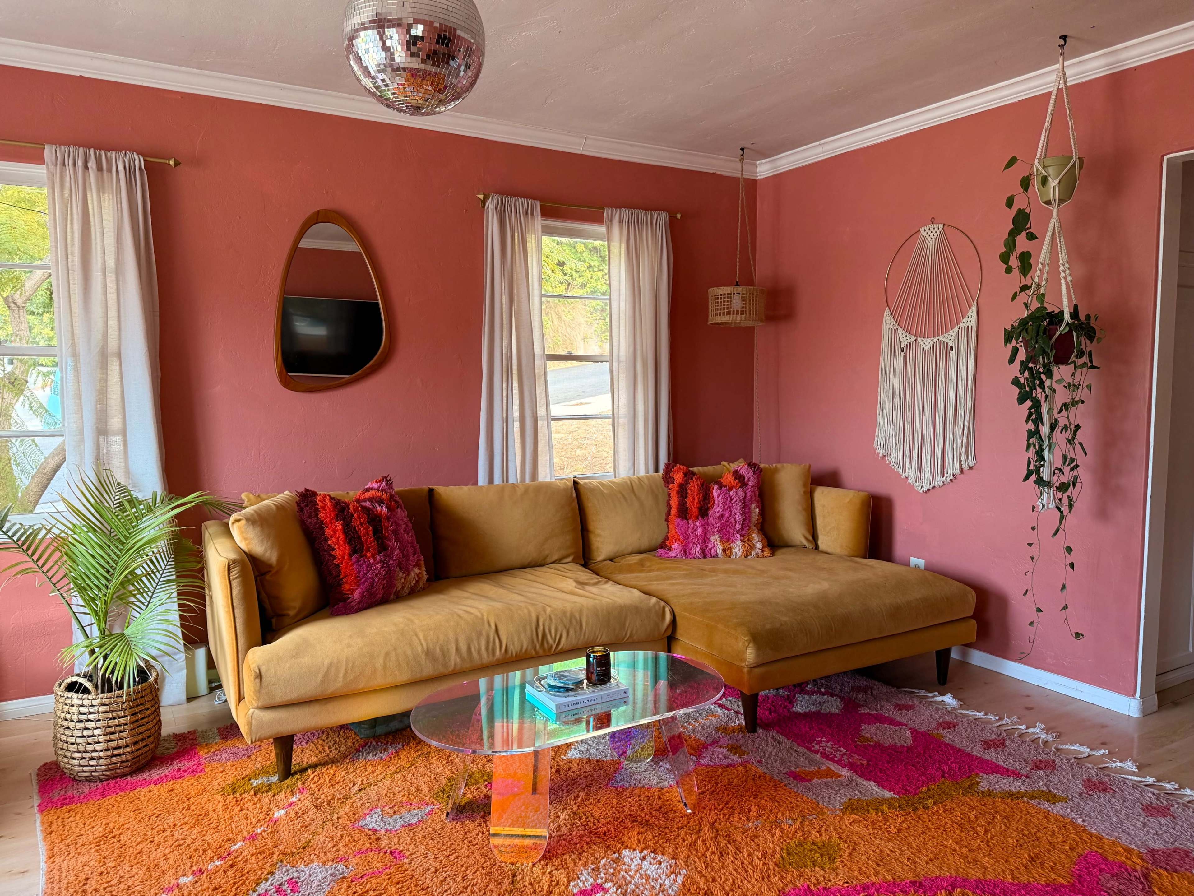The image shows a living room with a brown sectional couch, a round glass coffee table, a colorful area rug, and decorative elements on the walls.