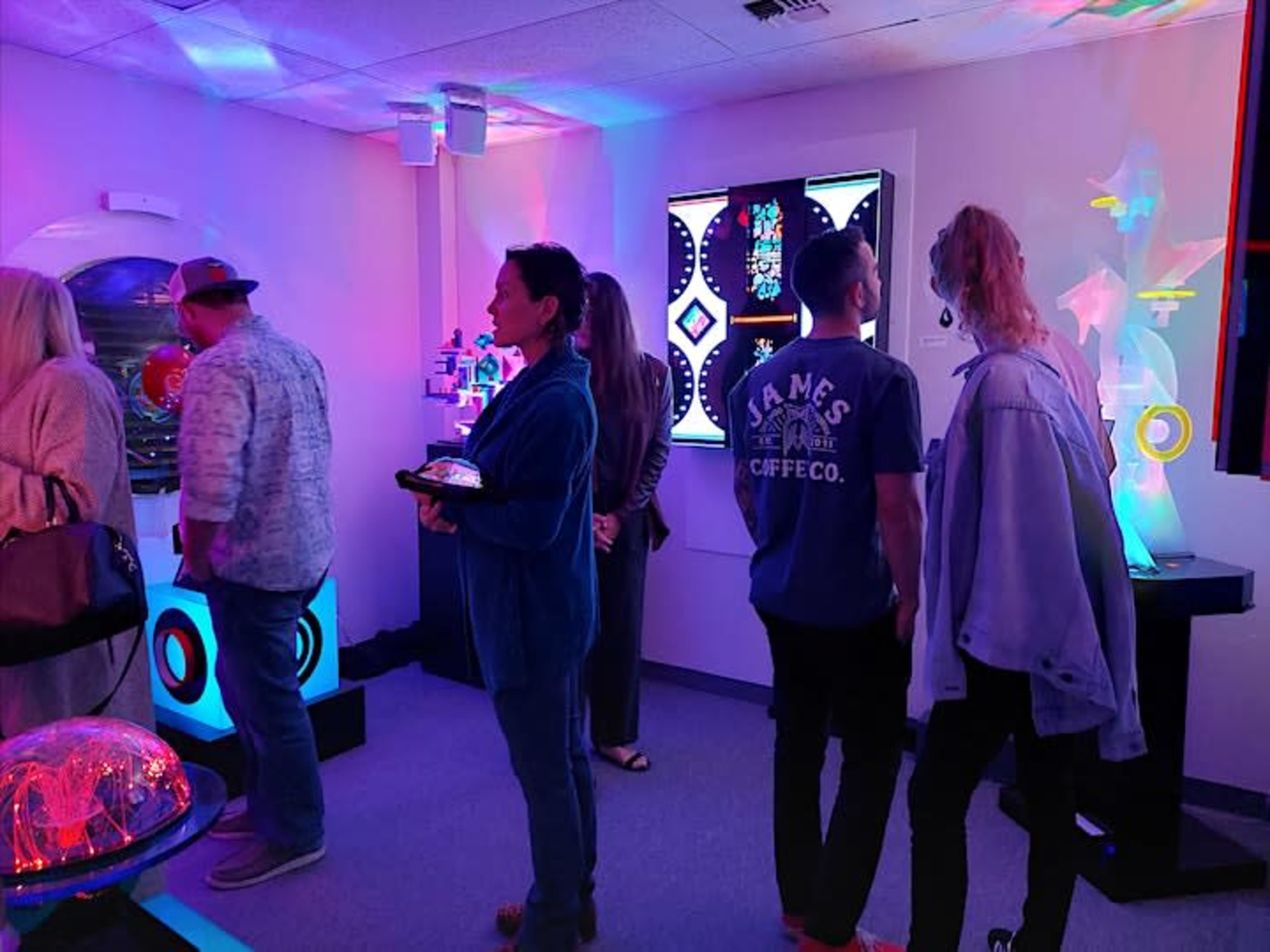 A group of people interacts with vibrant displays in a modern exhibition space.