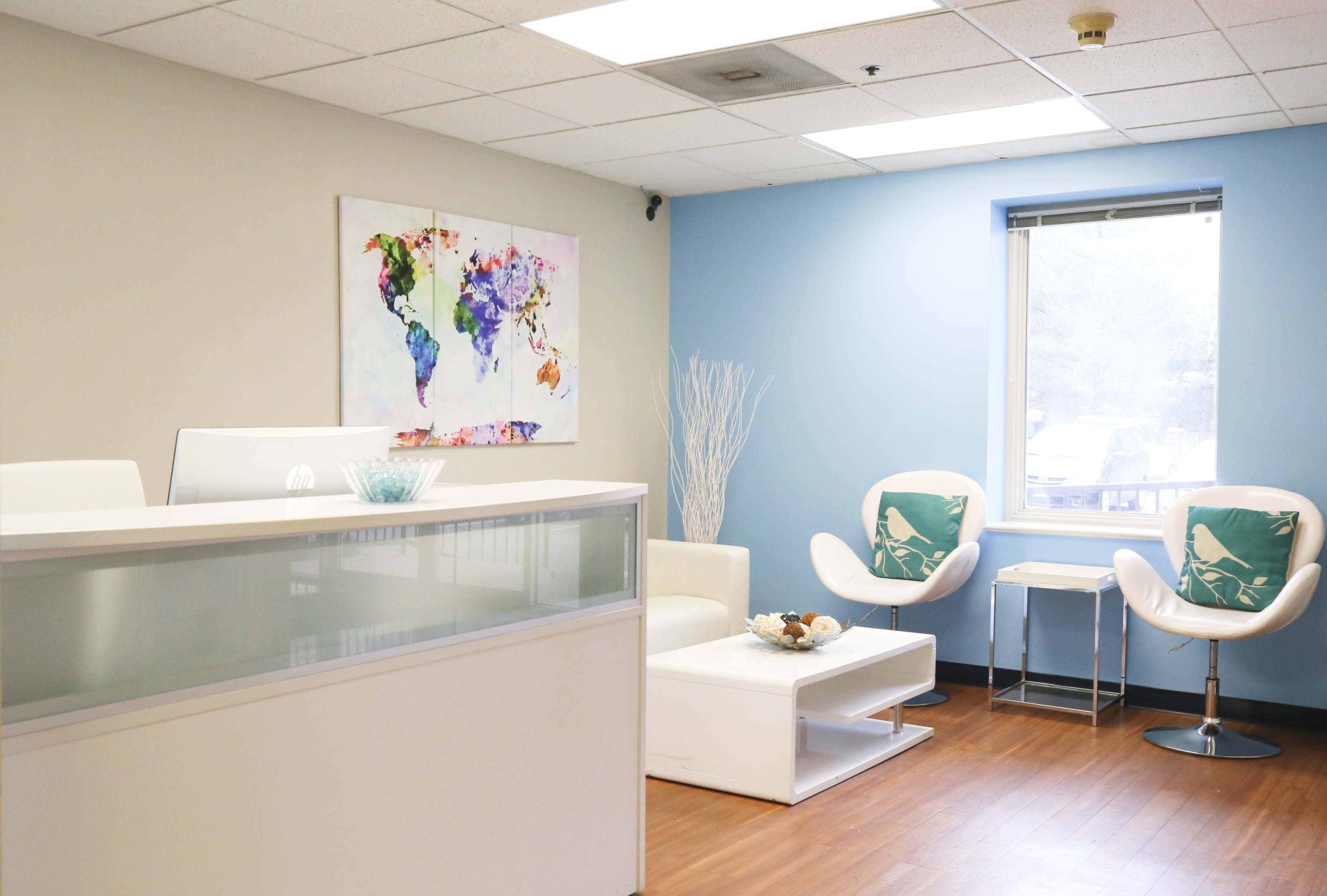 A modern office reception area with a white front desk, two white chairs with decorative cushions, and a colorful world map on the wall.