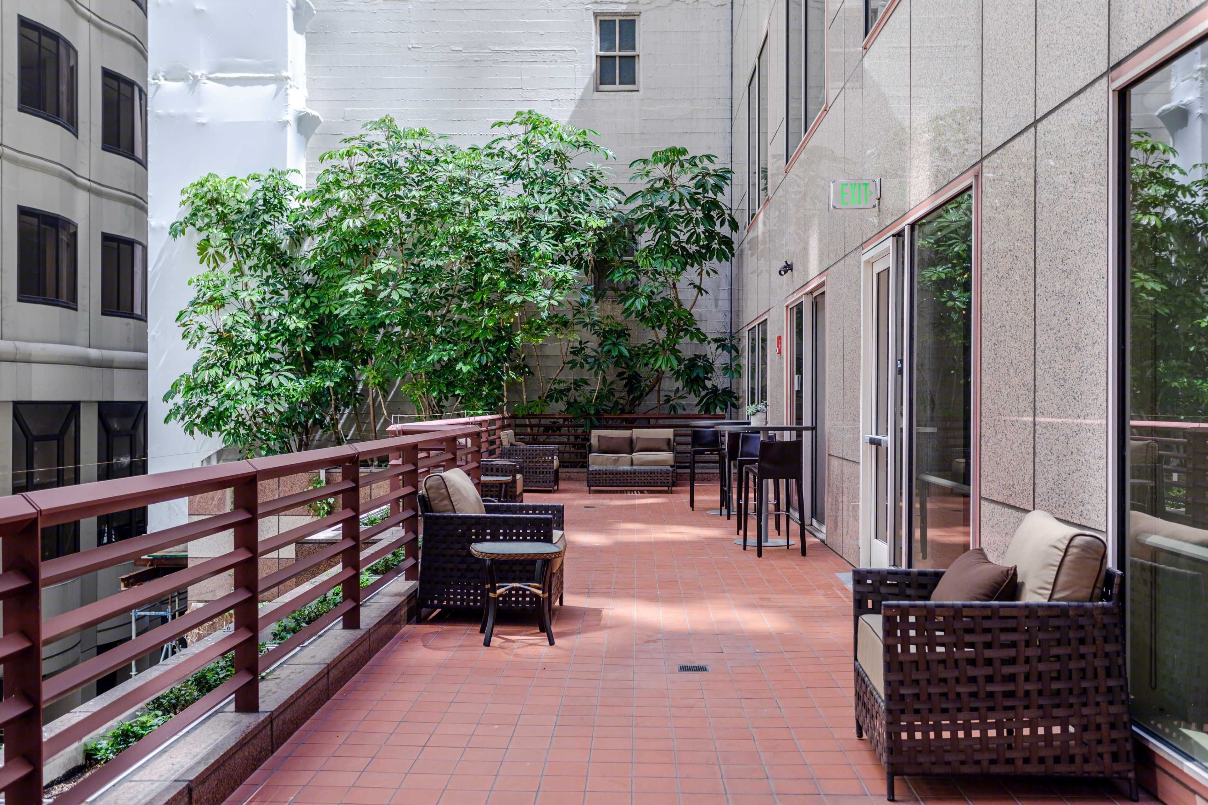 A balcony area with several seating arrangements surrounded by greenery and buildings.