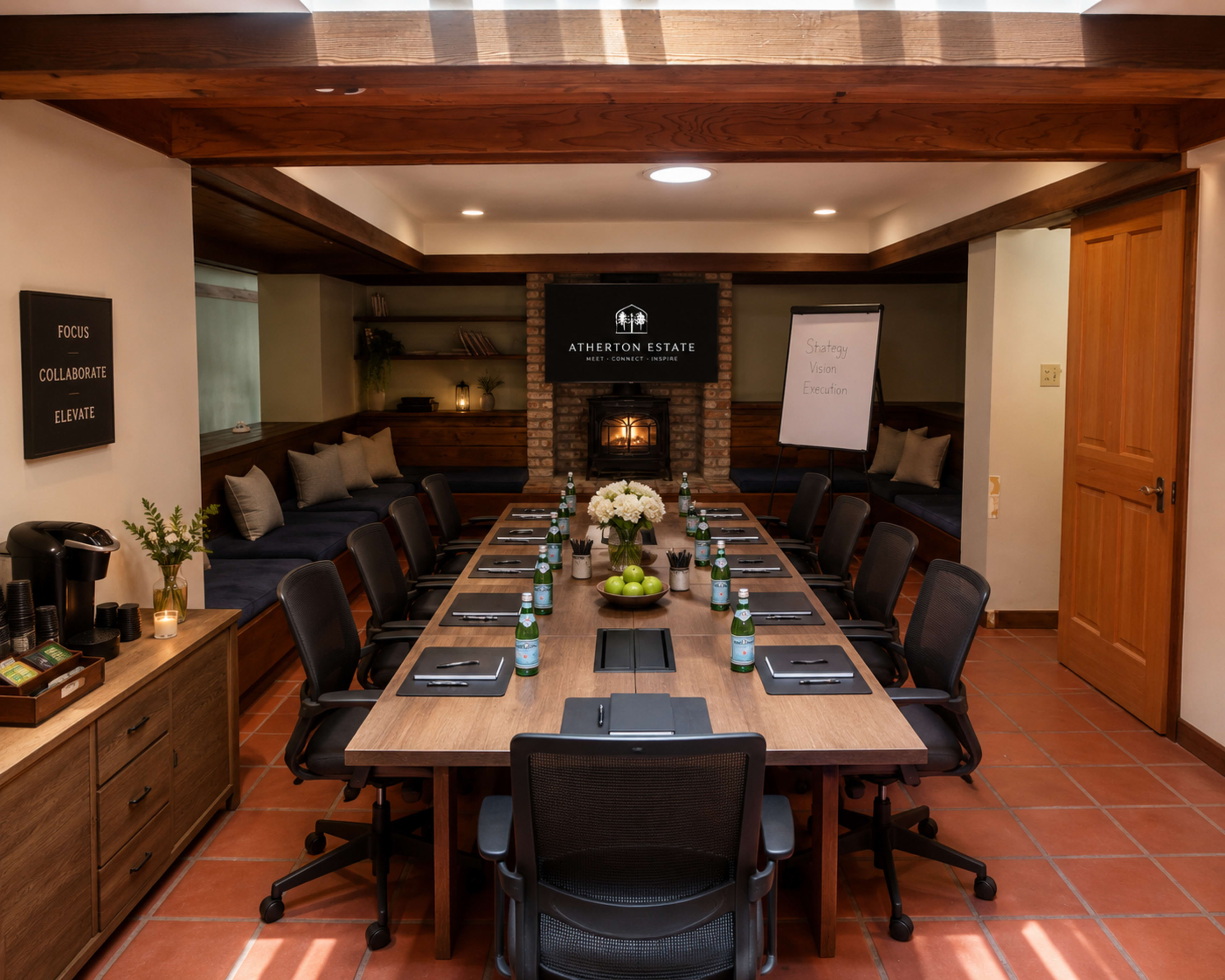 The image shows a spacious meeting room with a long wooden table arranged with chairs, water bottles, and stationery, accented by a fireplace and presentation board.