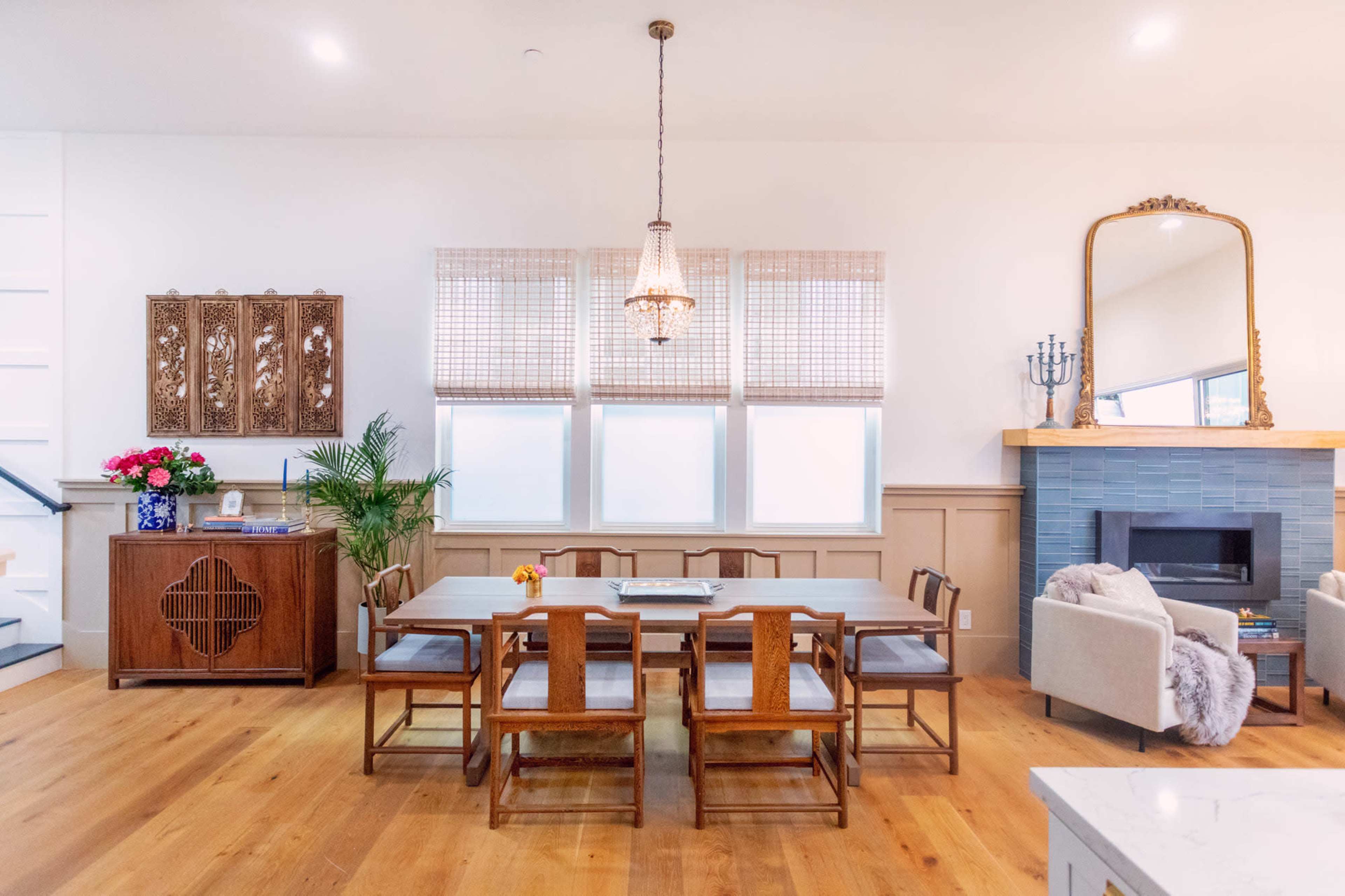 A spacious dining area features a large wooden table surrounded by chairs, with a minimalist decor including a chandelier and a fireplace.