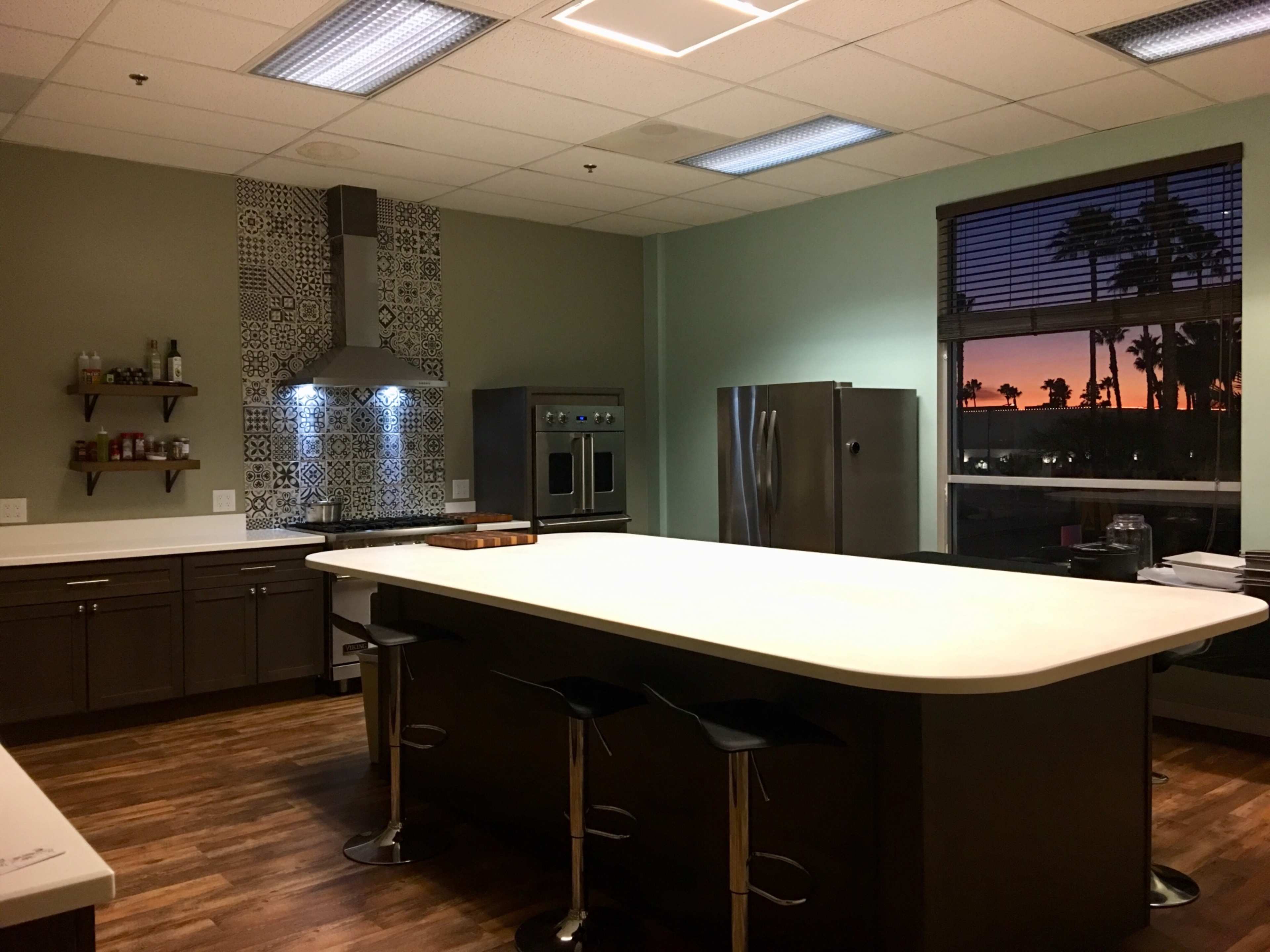 The kitchen features a large island, modern appliances, and a window showcasing a sunset.
