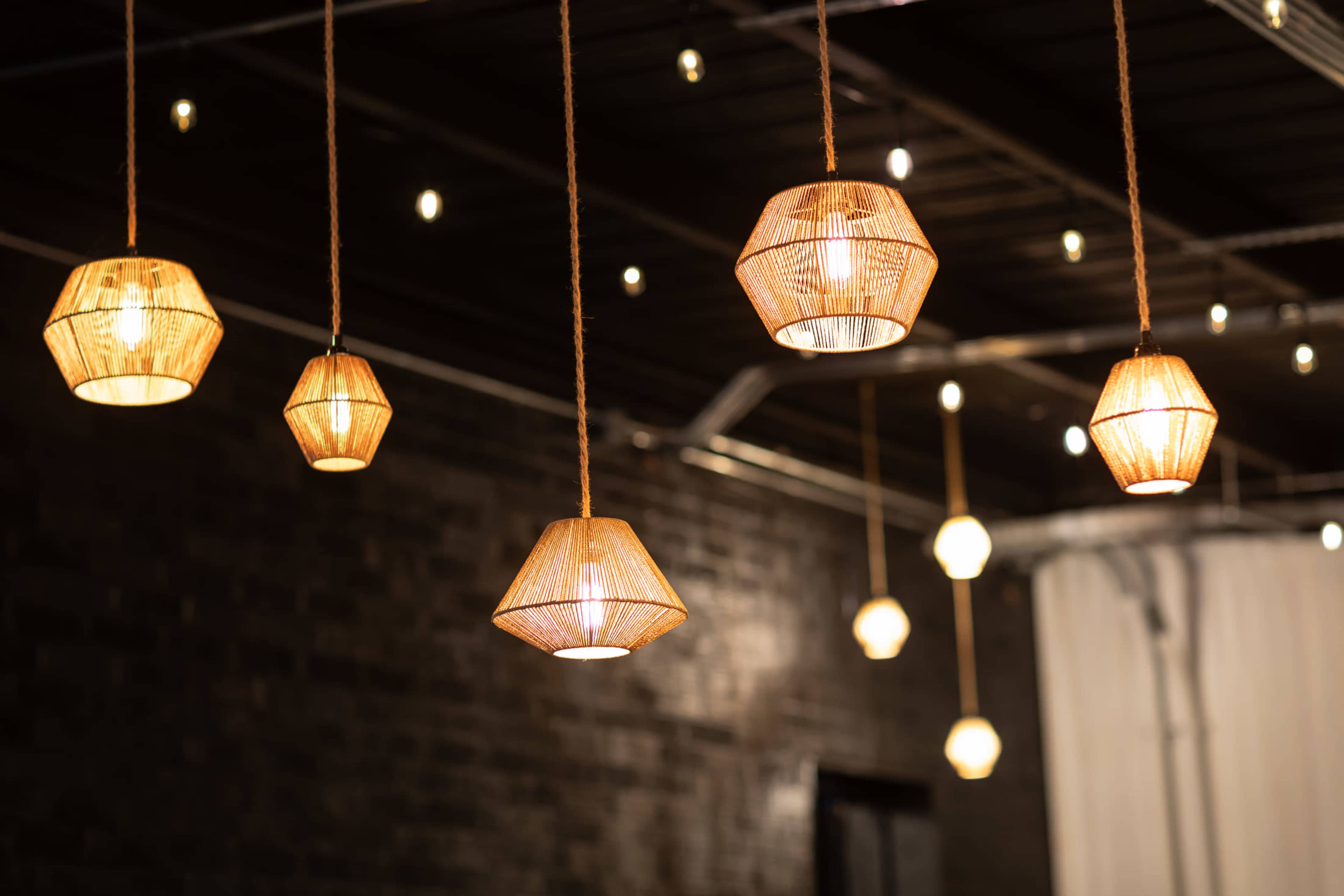 The image features several woven pendant lights hanging from a ceiling, with additional decorative string lights in the background.