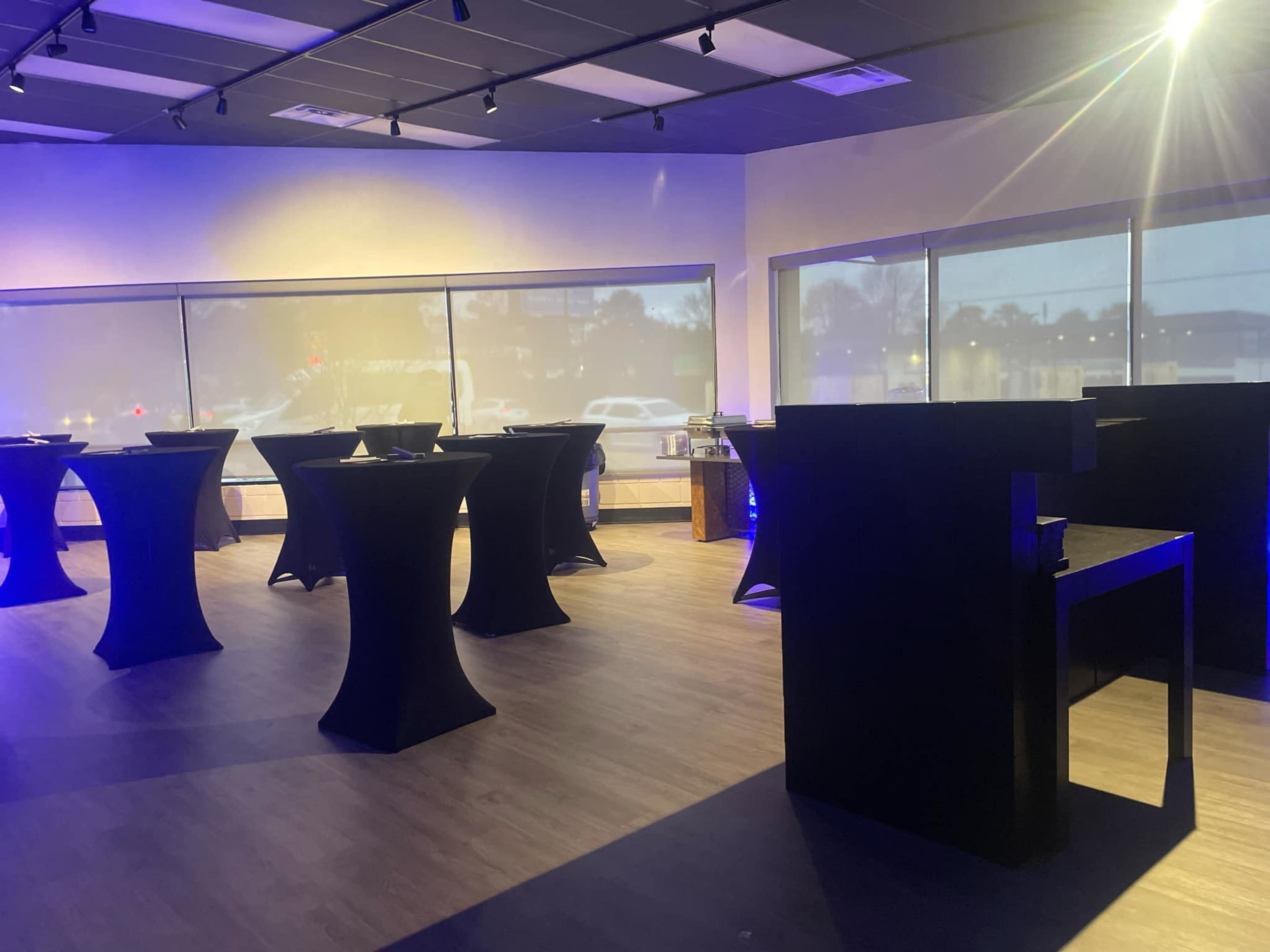 The image shows a modern event space with several tall tables arranged around a room with large windows and ambient lighting.