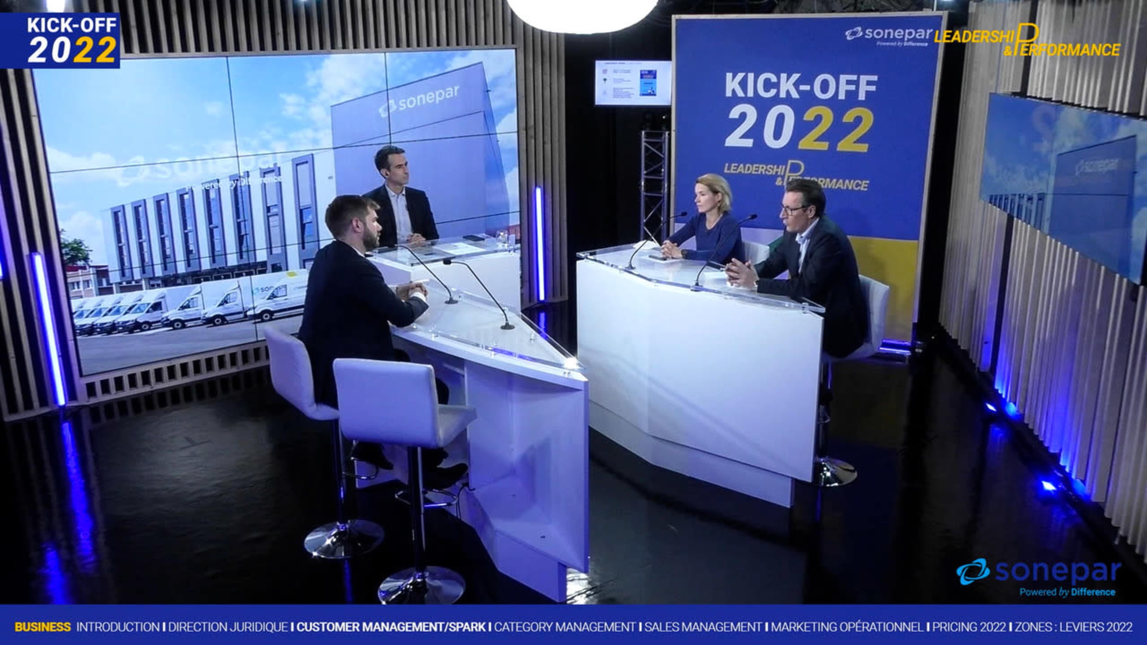 A panel of four people discusses business strategies in a modern studio setting, with a large graphic displaying "KICK-OFF 2022" in the background.