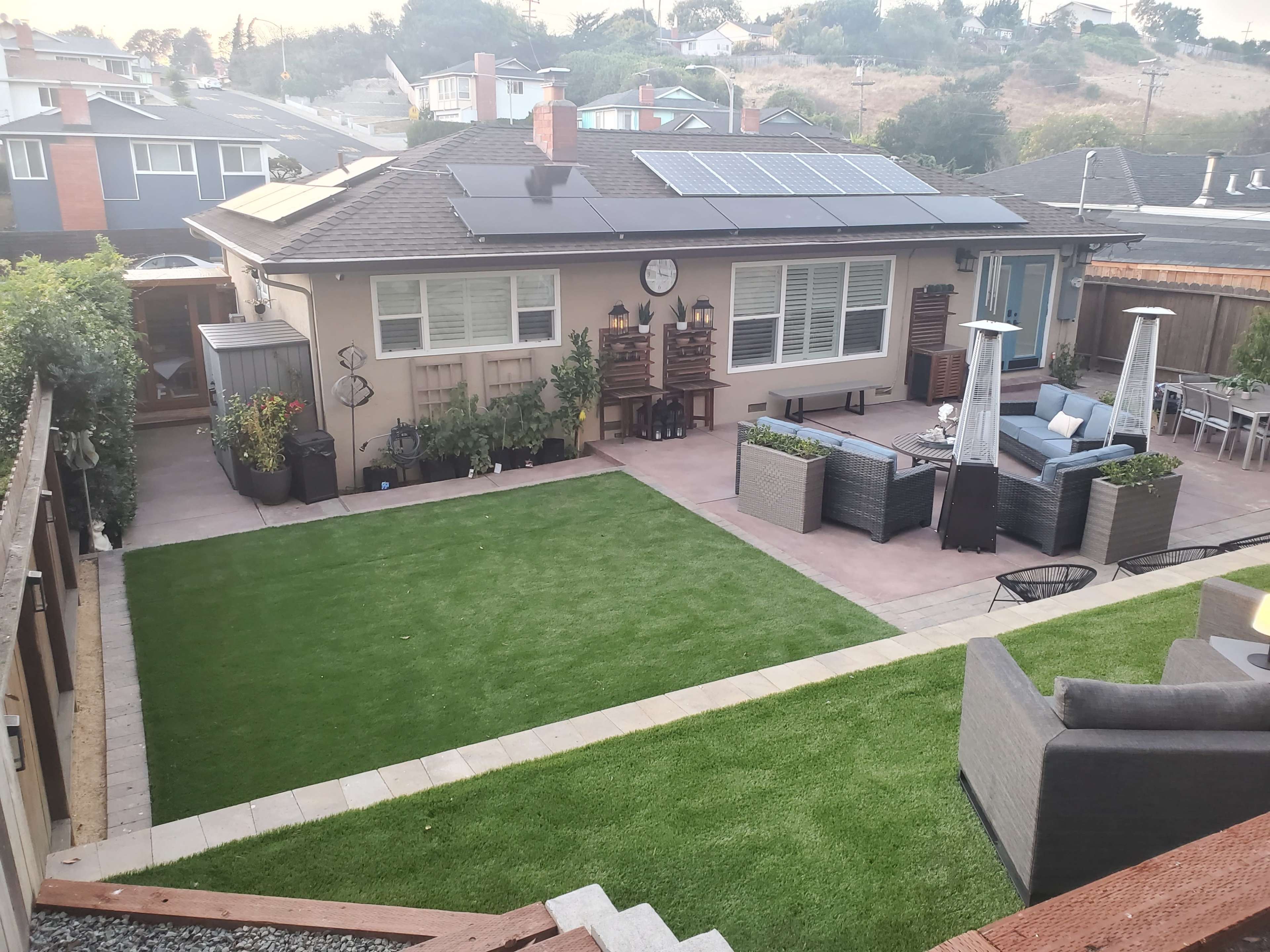 A landscaped backyard featuring artificial grass, a seating area with outdoor furniture, and a house equipped with solar panels on the roof.