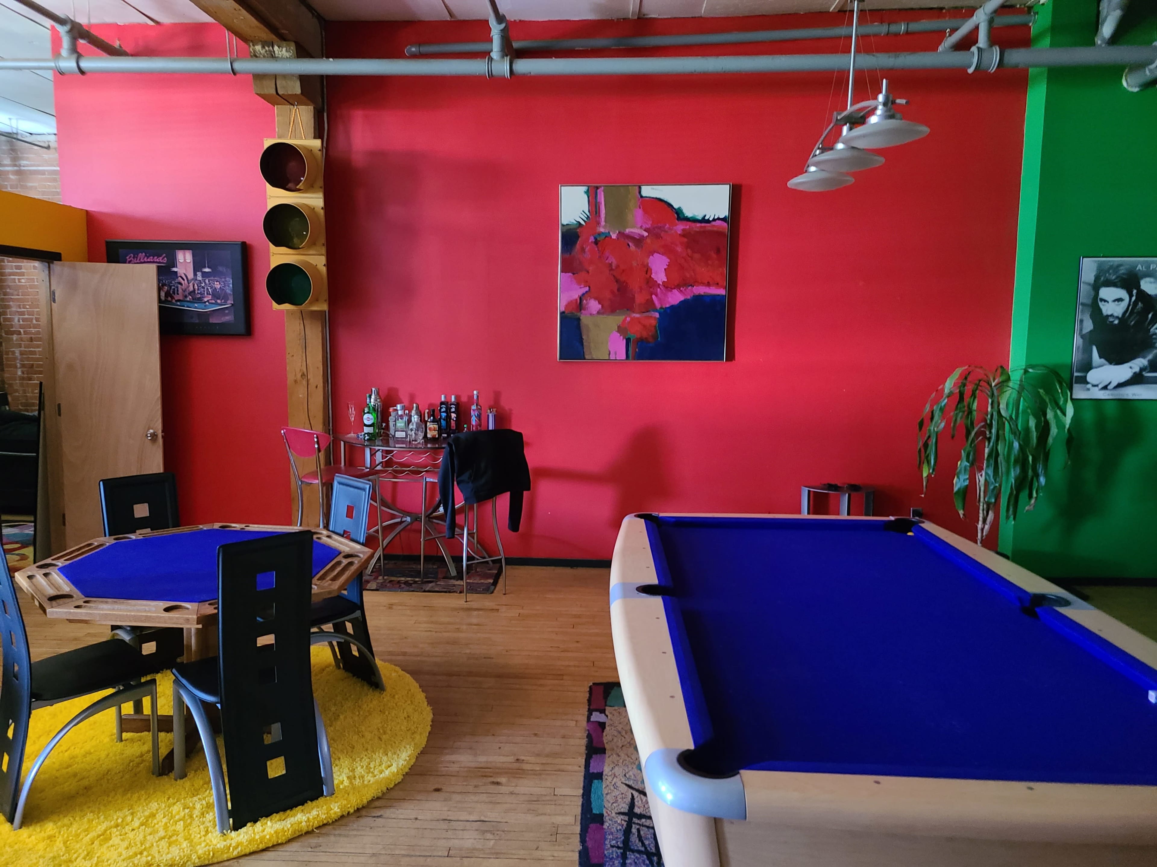 A room with a pool table, a round dining table, bar cart, and colorful walls, featuring red and green paint.