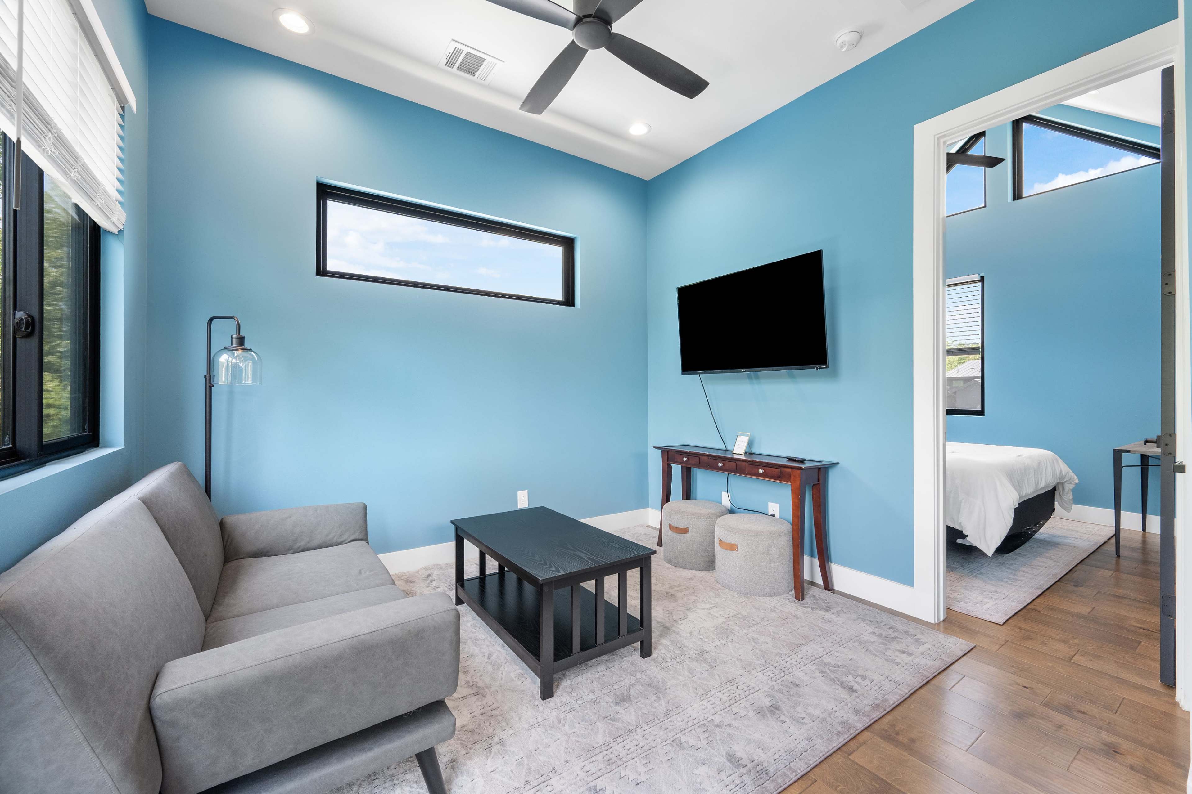 The image shows a modern, brightly colored room featuring a gray sofa, a black coffee table, and a wall-mounted television.