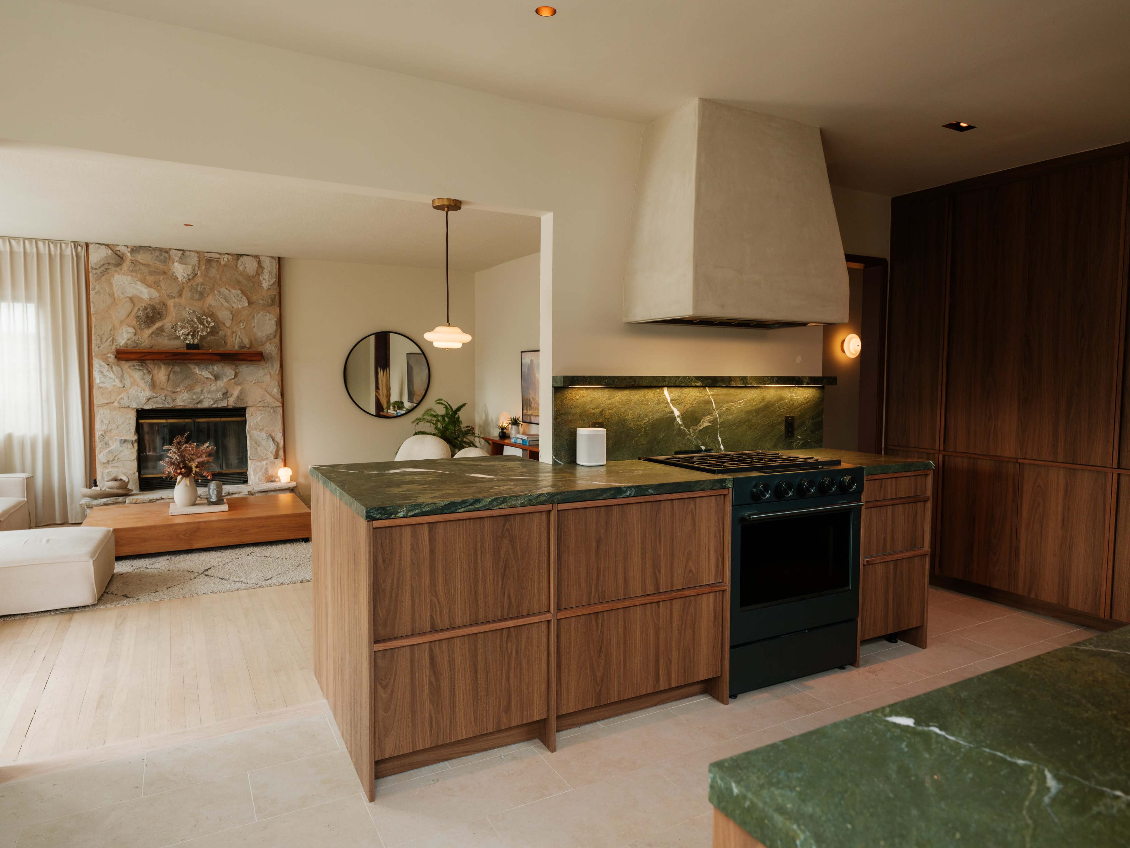 A modern kitchen features a green marble island and countertops, with wood cabinetry and an adjacent living area visible in the background.