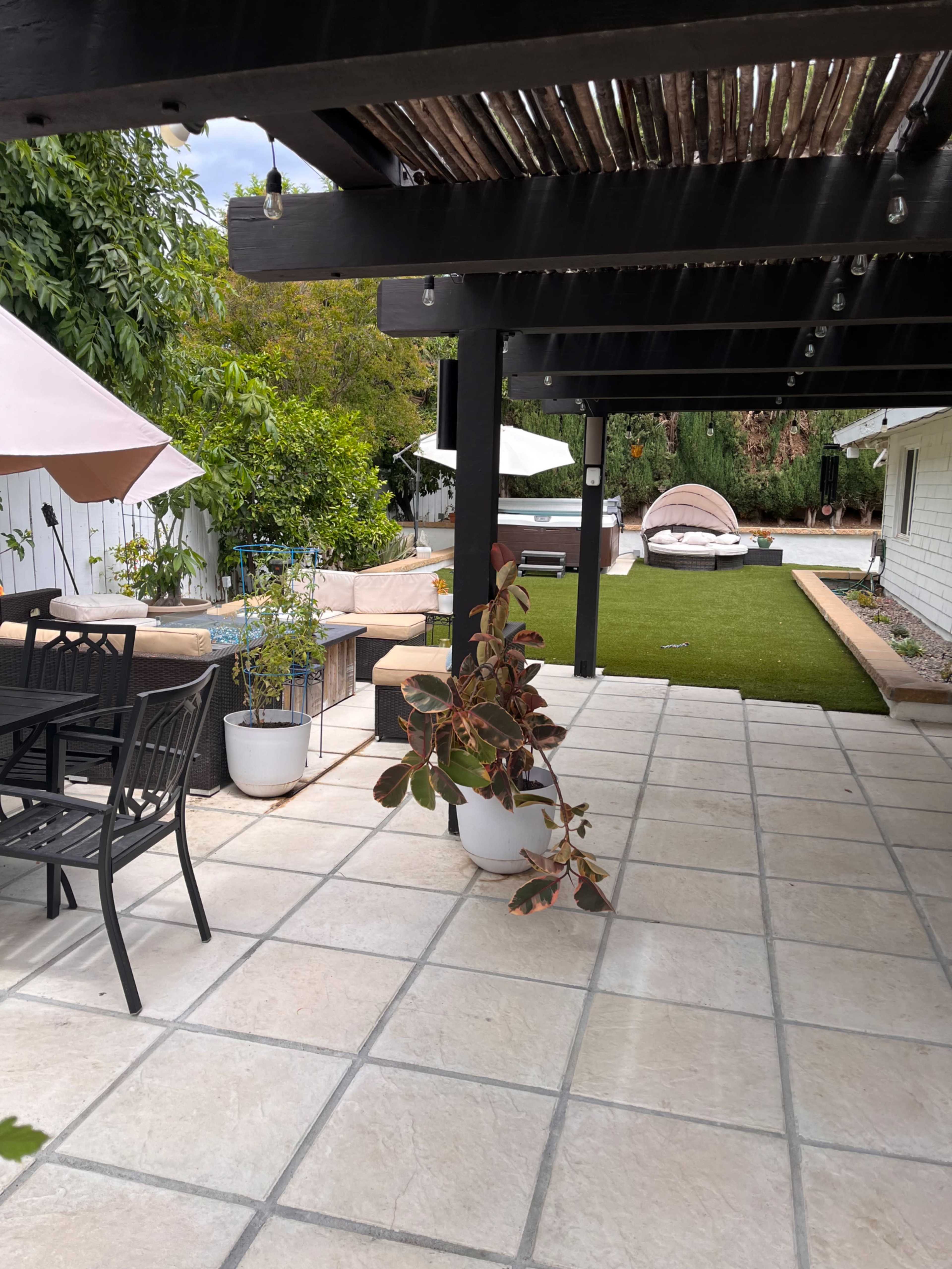 A neatly arranged outdoor patio with a table and chairs under a wooden pergola, leading to a grassy area with lounge chairs and a shaded seating space.