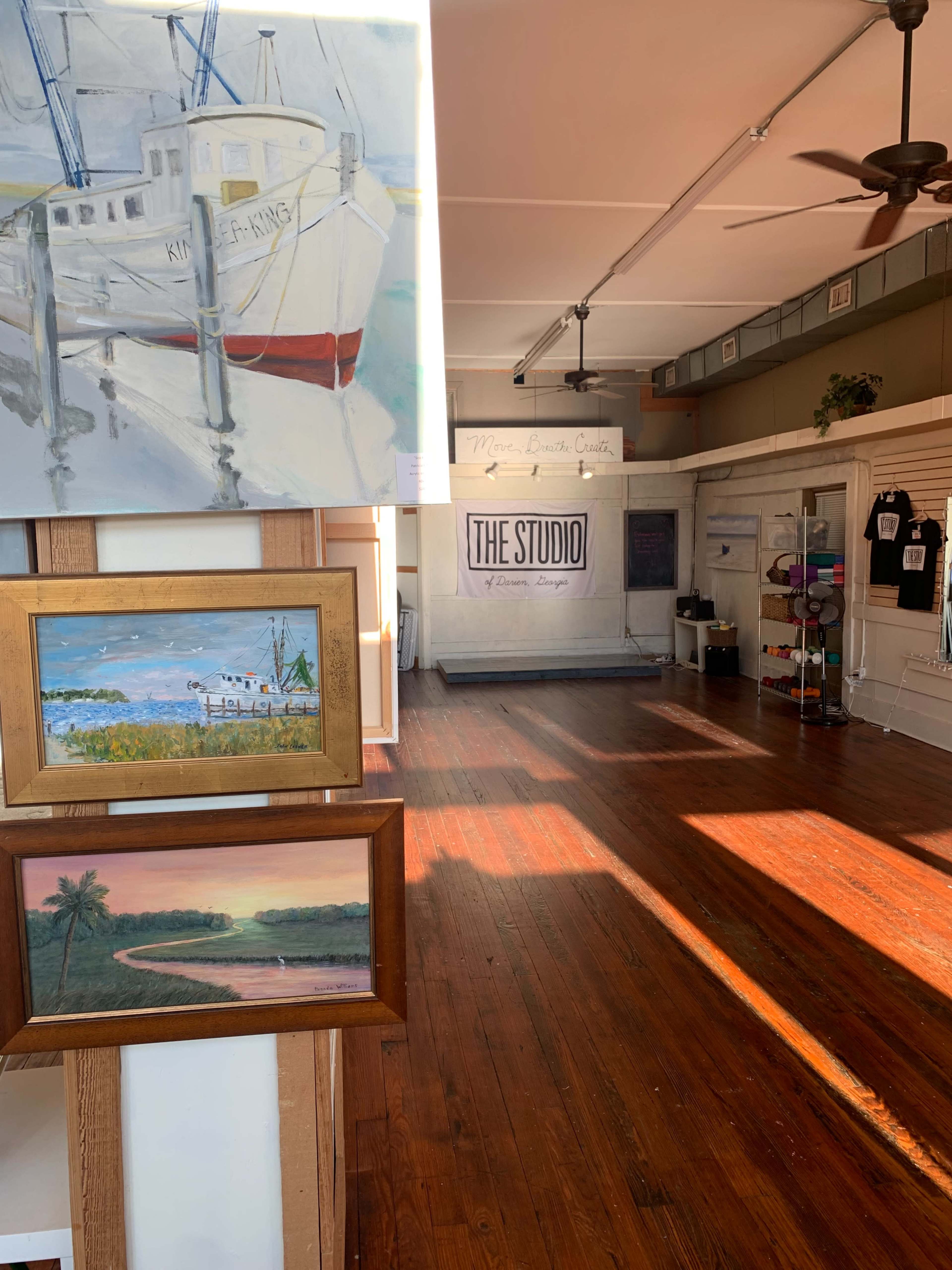The image shows an art studio with wooden floors, featuring paintings on the wall and a large banner that reads "THE STUDIO."