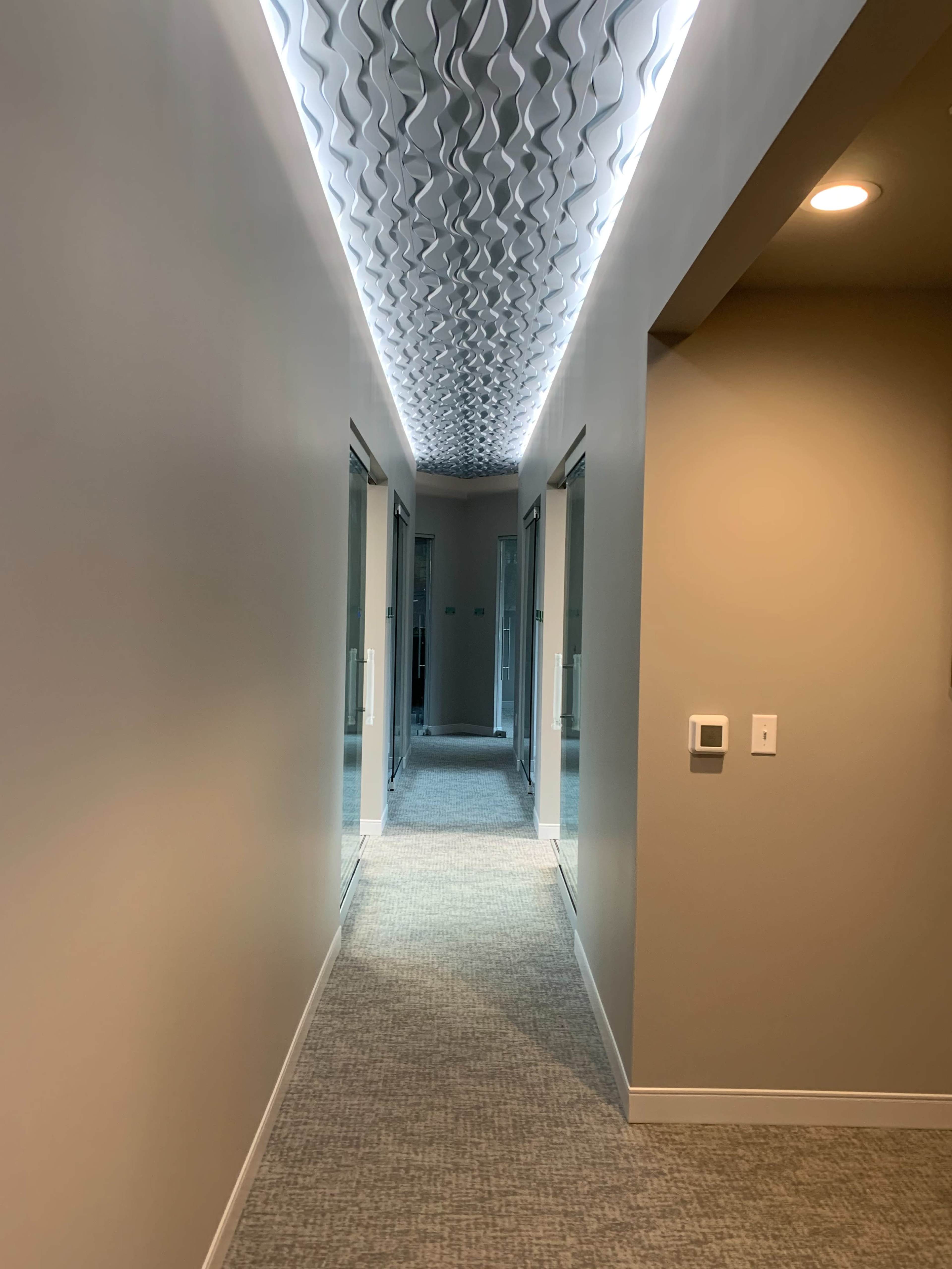 A well-lit corridor features textured ceiling panels and mirrored doors along the walls.