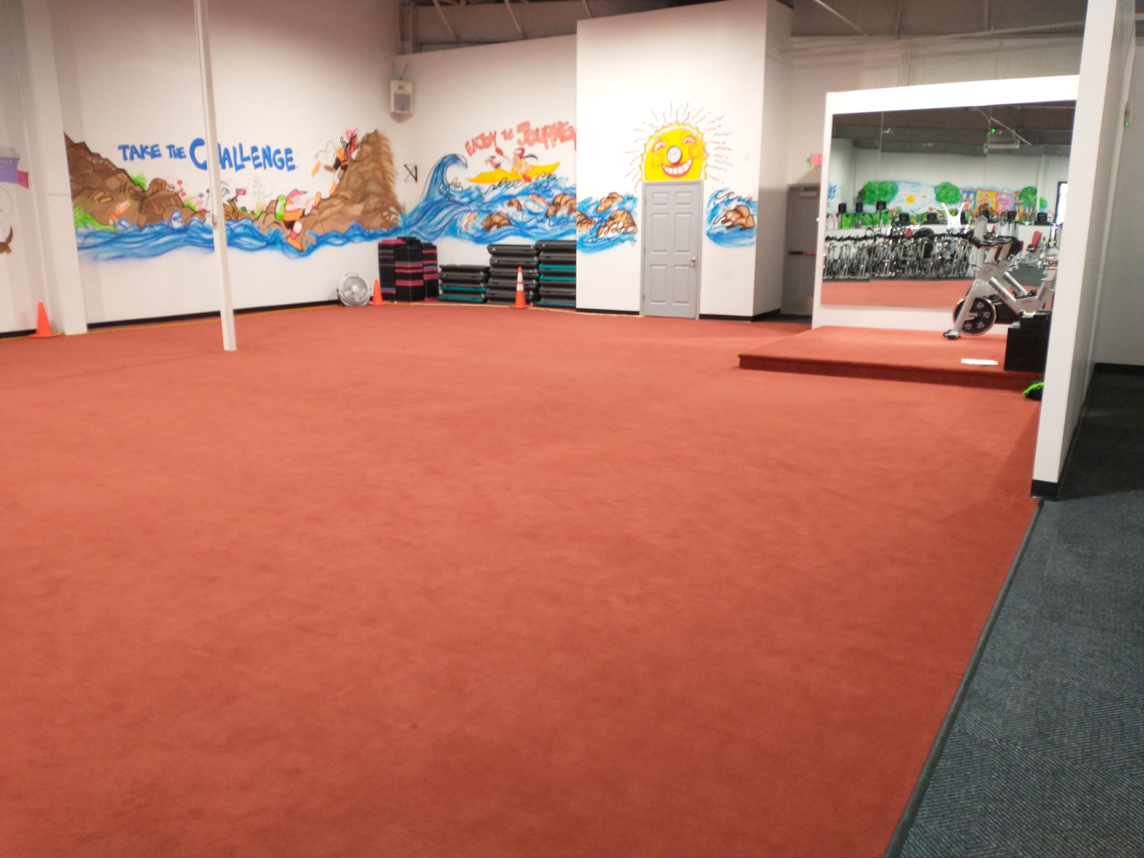 An empty fitness space with red carpet flooring and colorful murals on the walls, including a sun and waves.