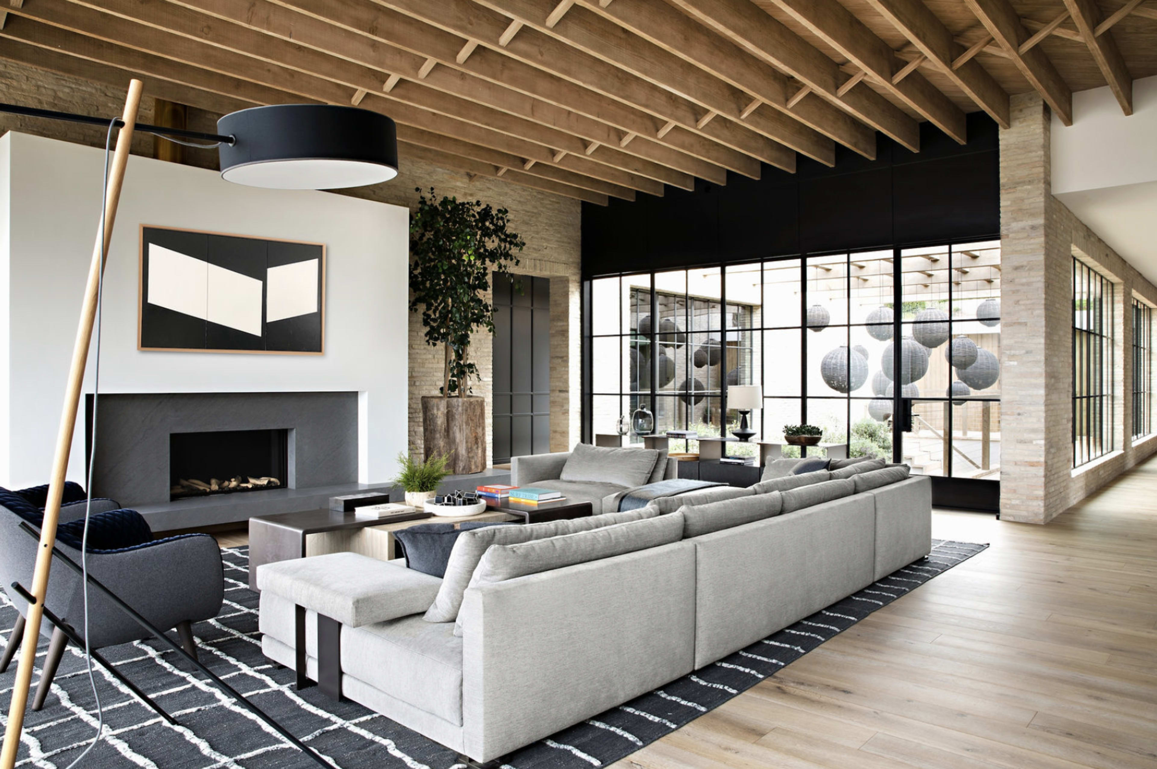 A spacious living room with a modern design, featuring a large sectional sofa, a fireplace, and large windows that overlook an outdoor space.