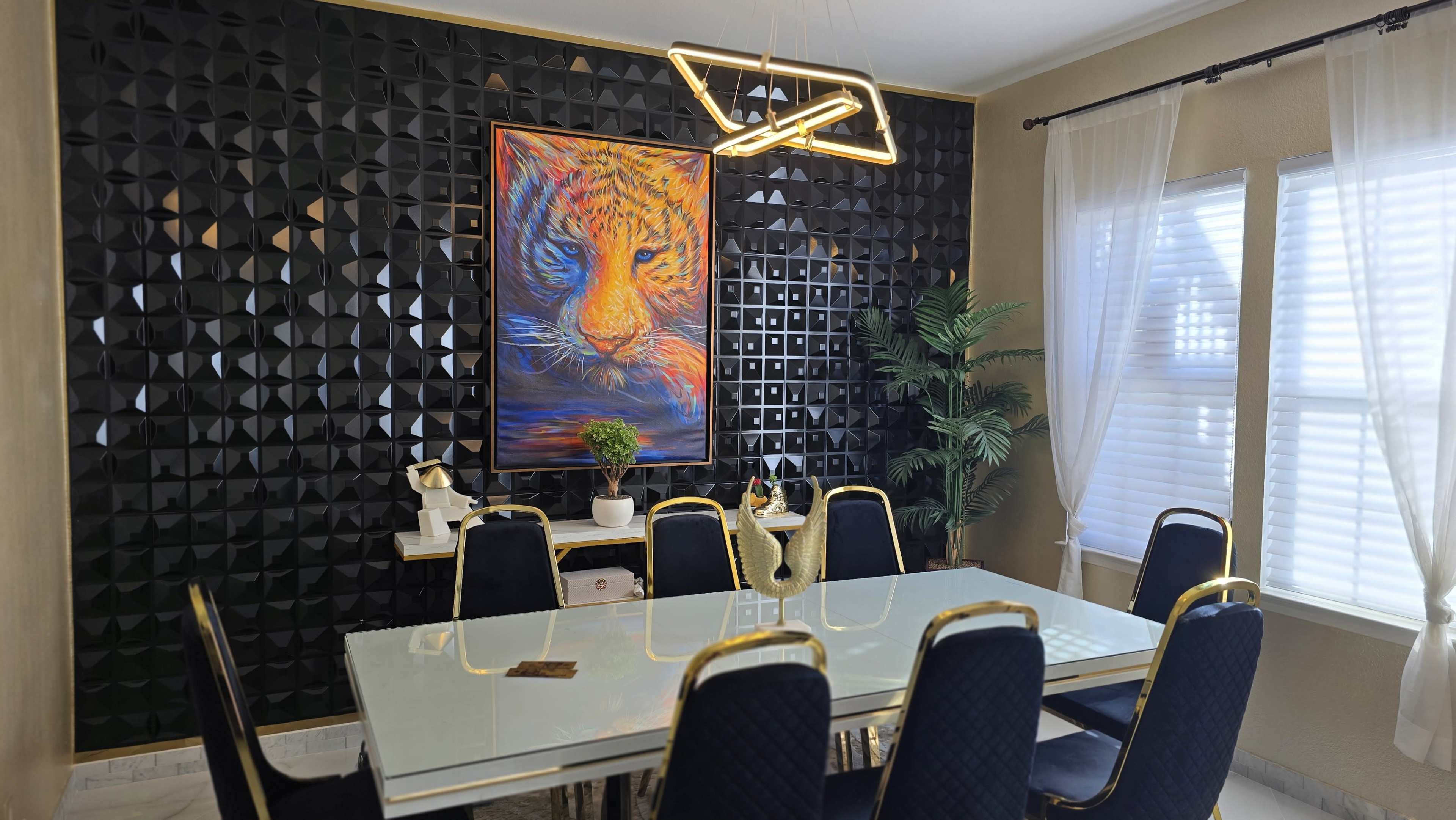 A modern dining room features a large glass table surrounded by navy blue chairs, with a striking lion portrait on a black textured wall and a potted plant in the corner.