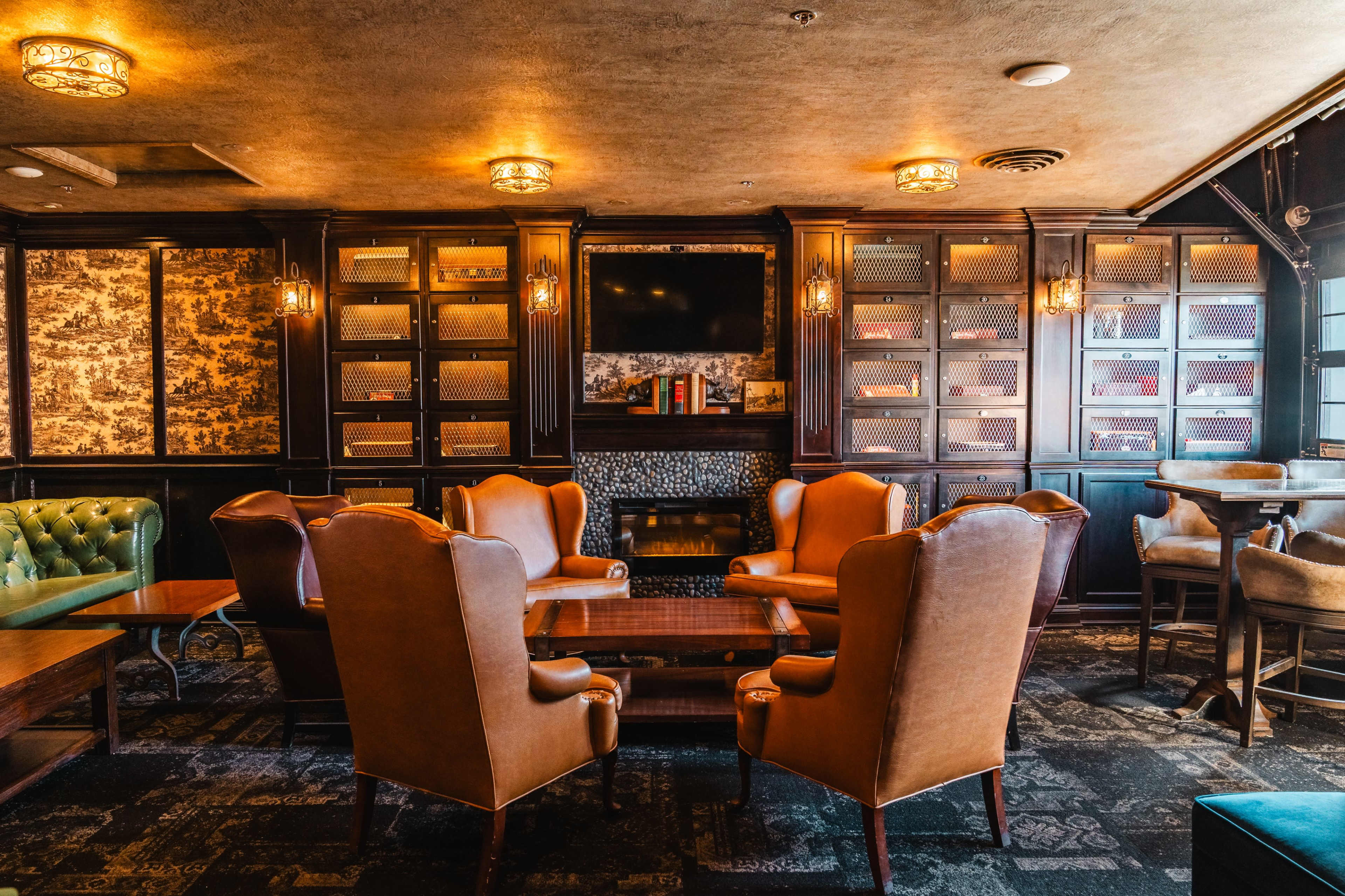 The image shows a cozy lounge area with leather armchairs arranged around a wooden coffee table, set against a backdrop of dark wood paneling and decorative lighting.