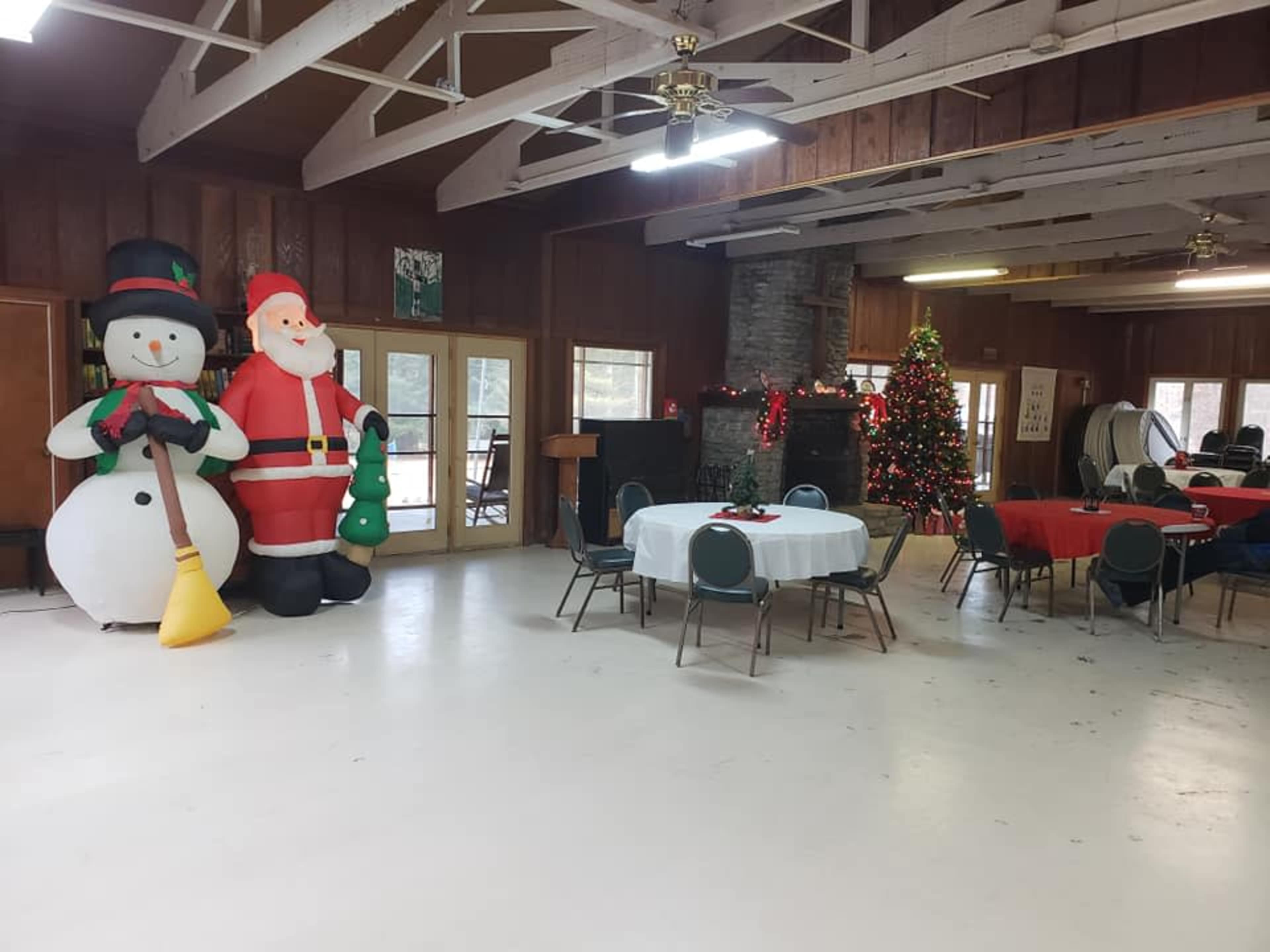 The interior of a decorated hall features inflatable Christmas decorations, including a snowman and Santa Claus, alongside tables set for a festive gathering and a Christmas tree.