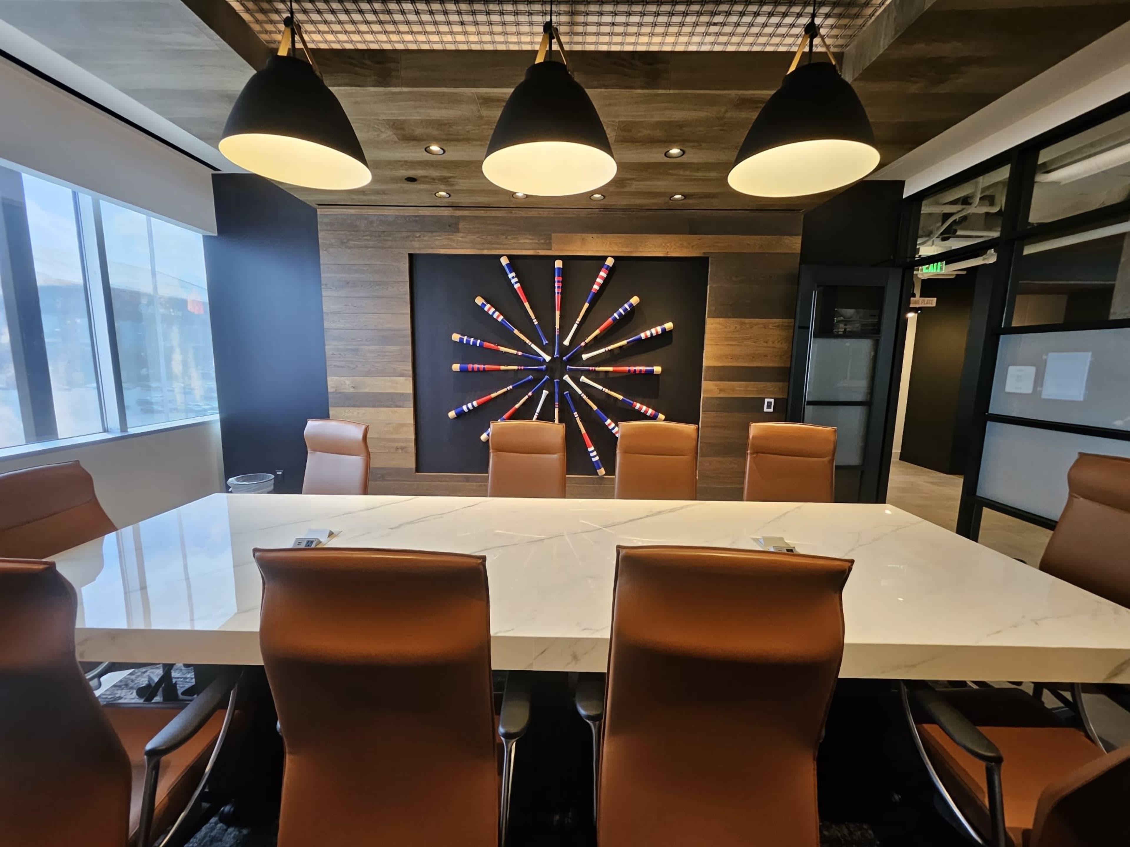 A modern conference room features a long marble table surrounded by brown leather chairs, with a decorative wall displaying a colorful starburst arrangement of art.