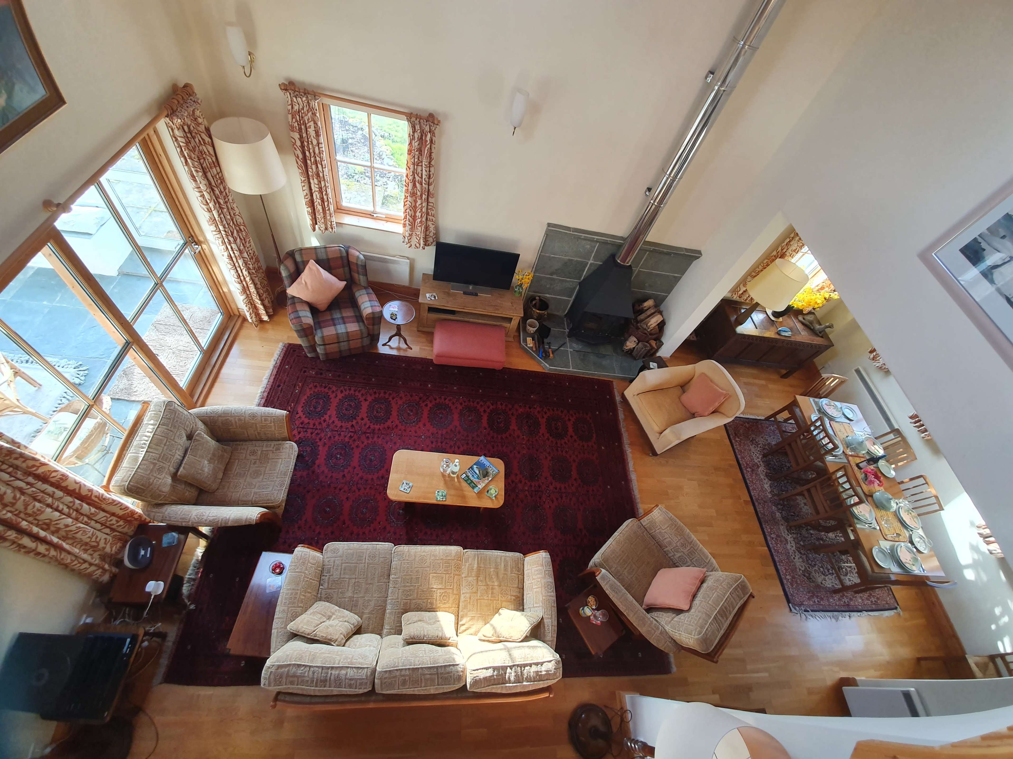 A spacious living room features two light-colored sofas, a coffee table, and a dining area with a wooden table, surrounded by large windows and a patterned rug.