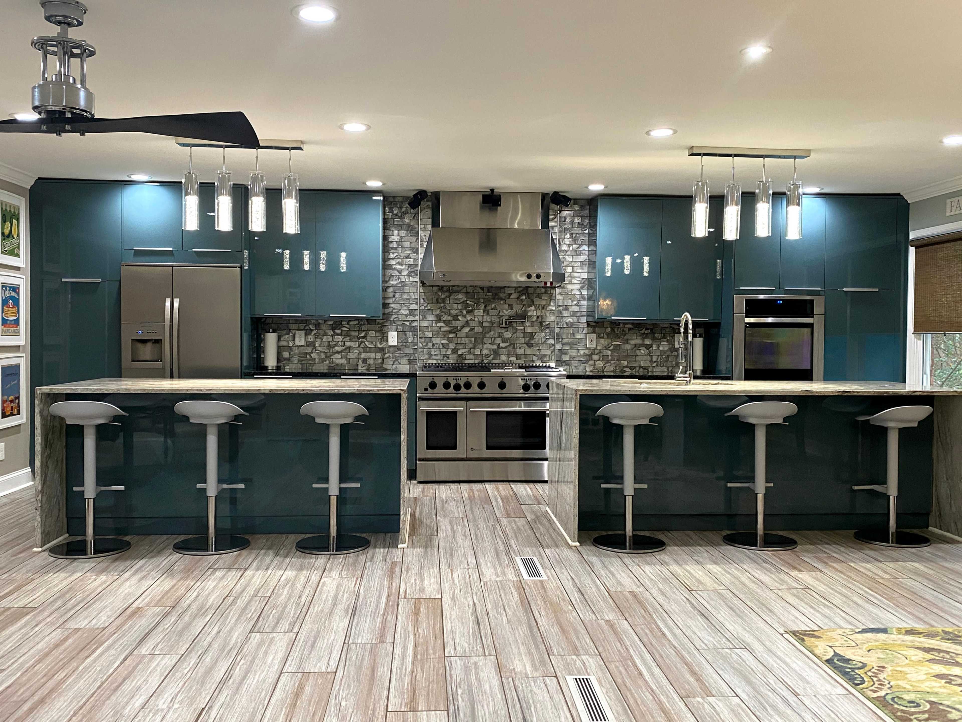 The image shows a modern kitchen with teal cabinets, a stainless steel stove, and a large island with four white bar stools.