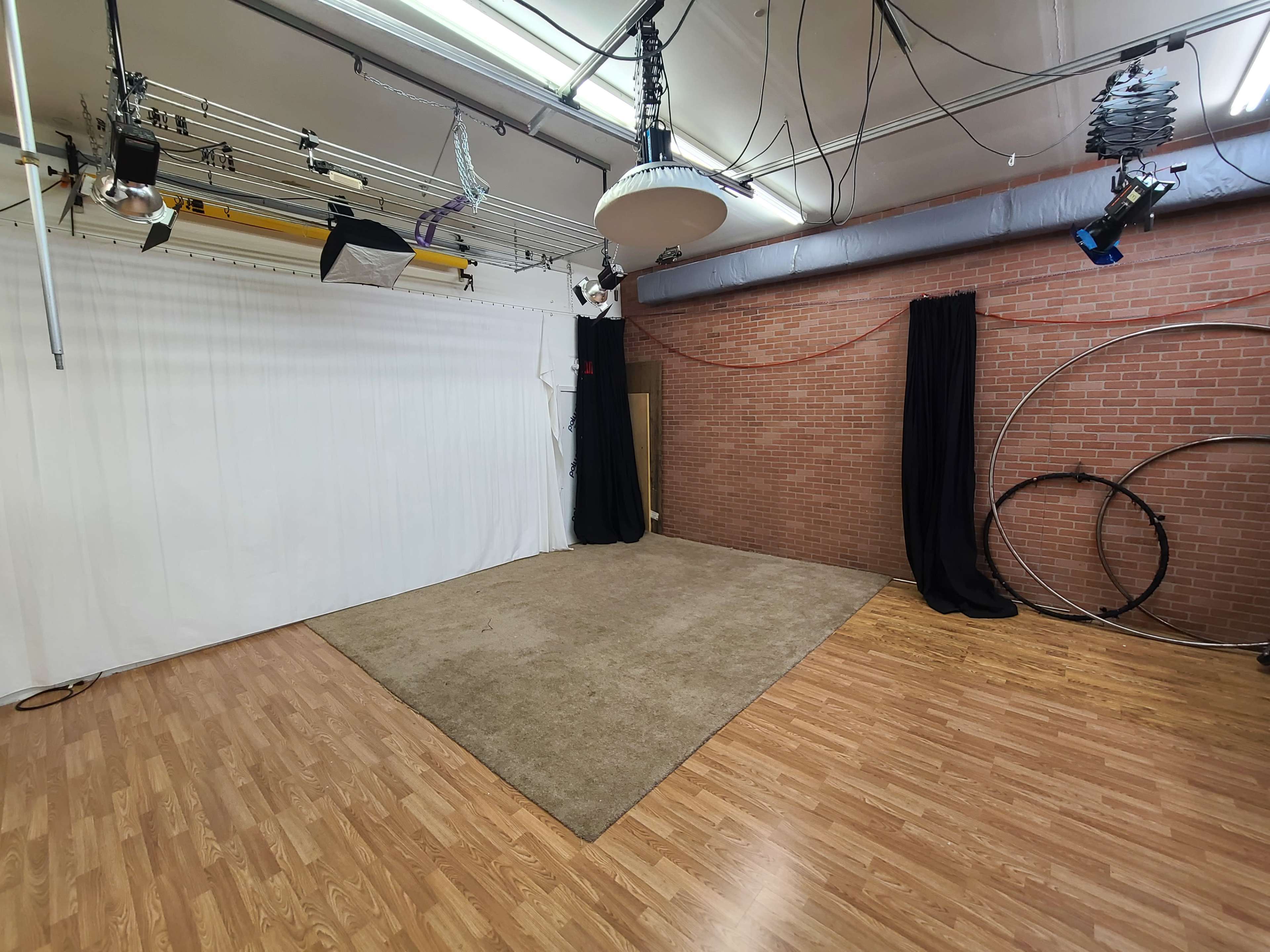 A spacious photography studio featuring a white backdrop, a carpeted area, and various lighting equipment hanging from the ceiling.