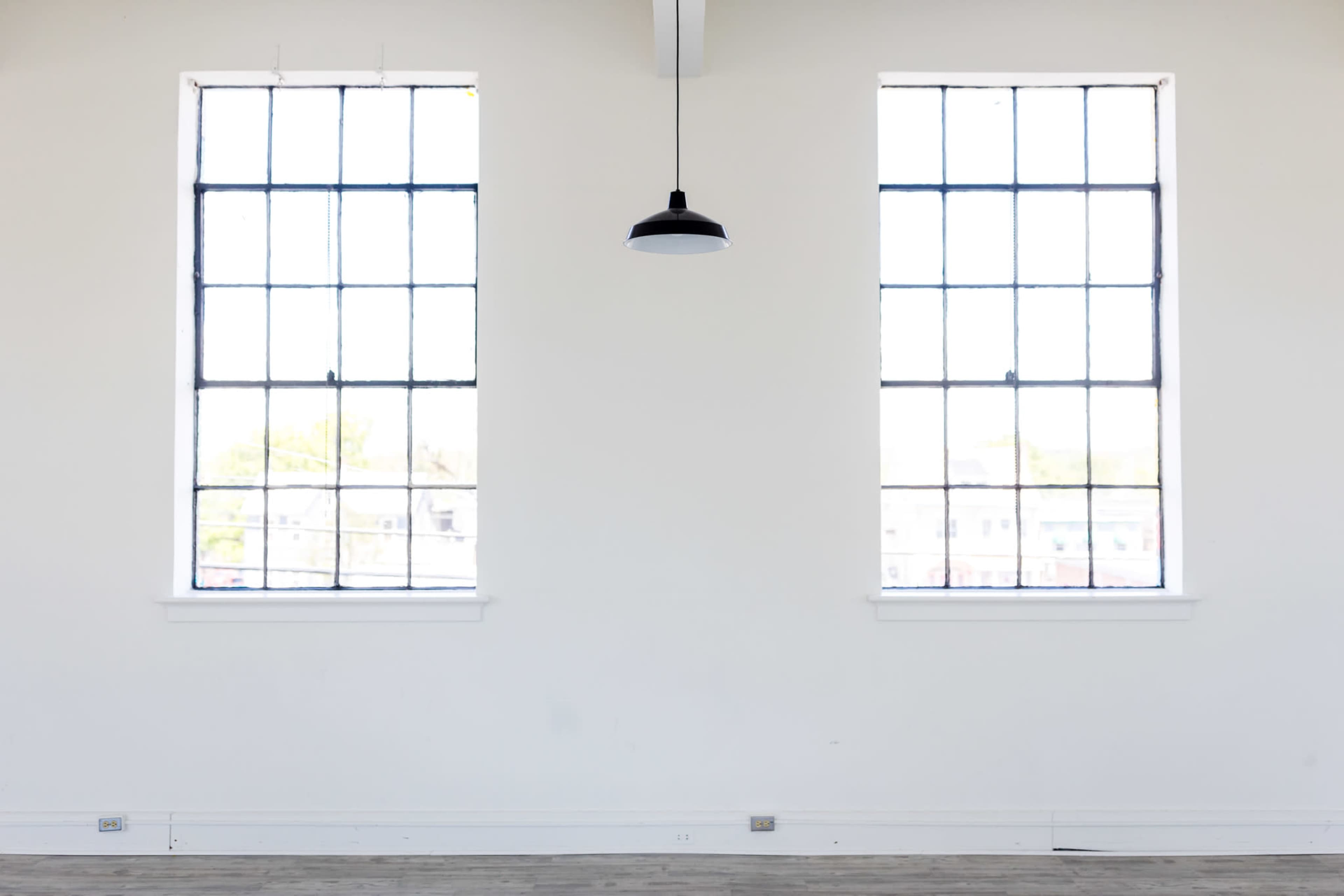 An empty room with two large windows and a pendant light fixture hanging from the ceiling.