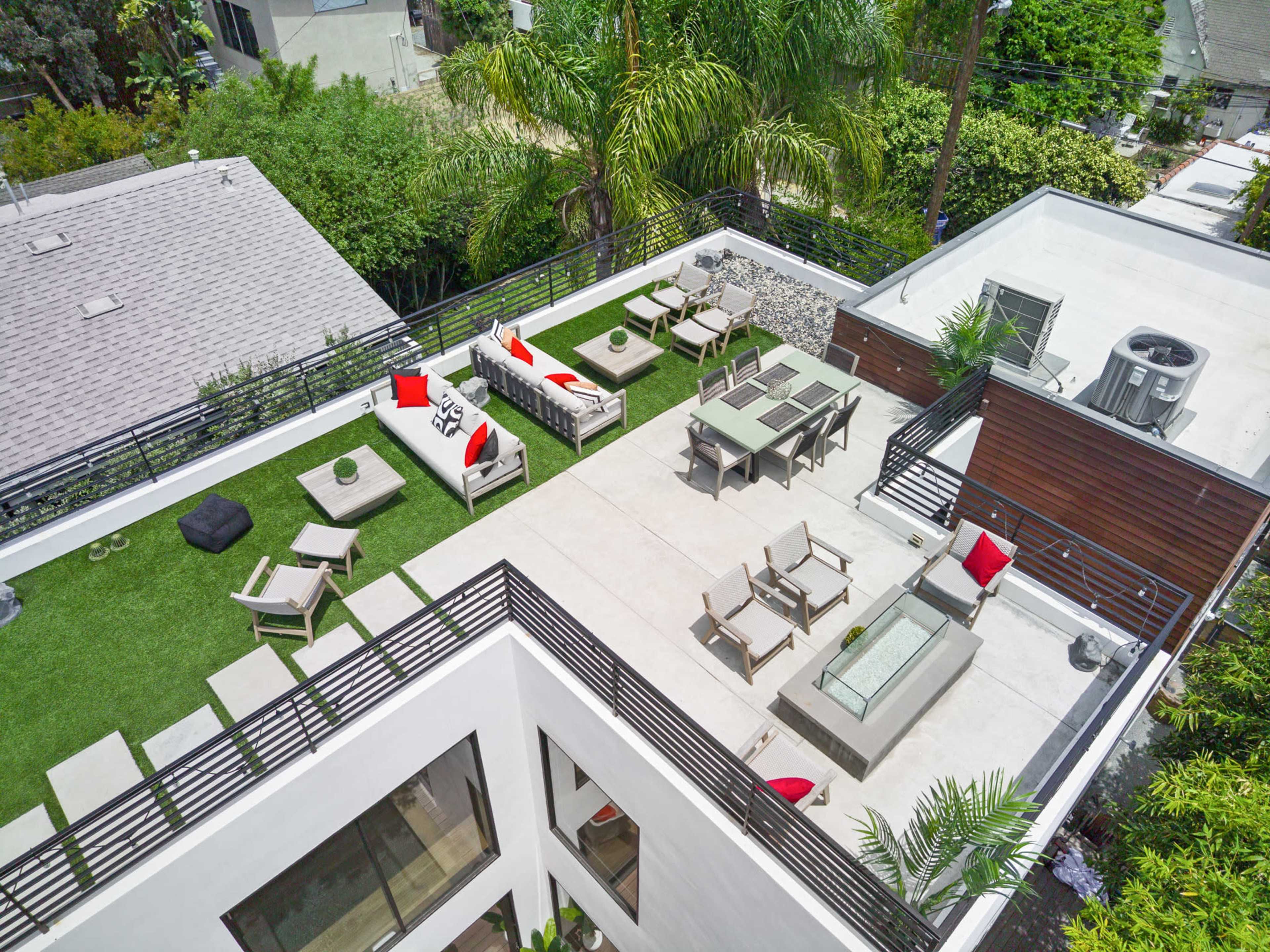 A spacious rooftop terrace featuring seating areas, outdoor furniture, and landscaping with green grass and palm trees.