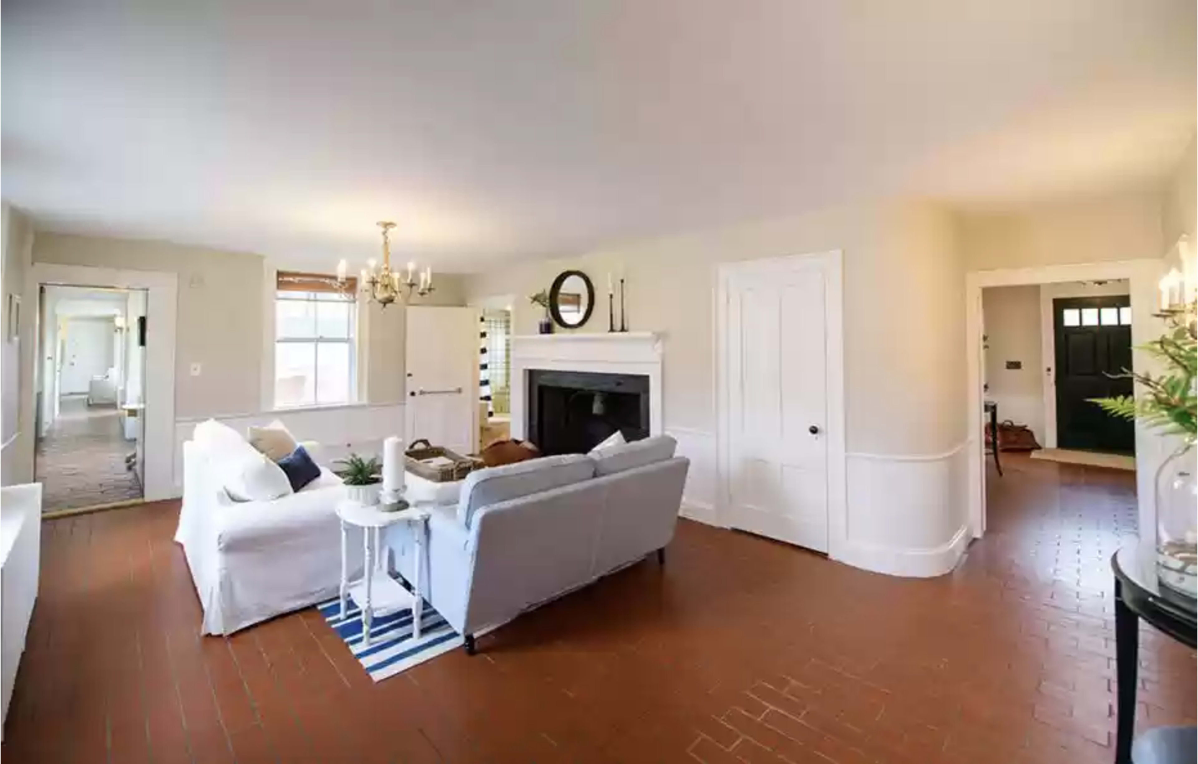 The image shows a well-lit living room featuring a white sofa, a fireplace, and a dark door leading to another room.