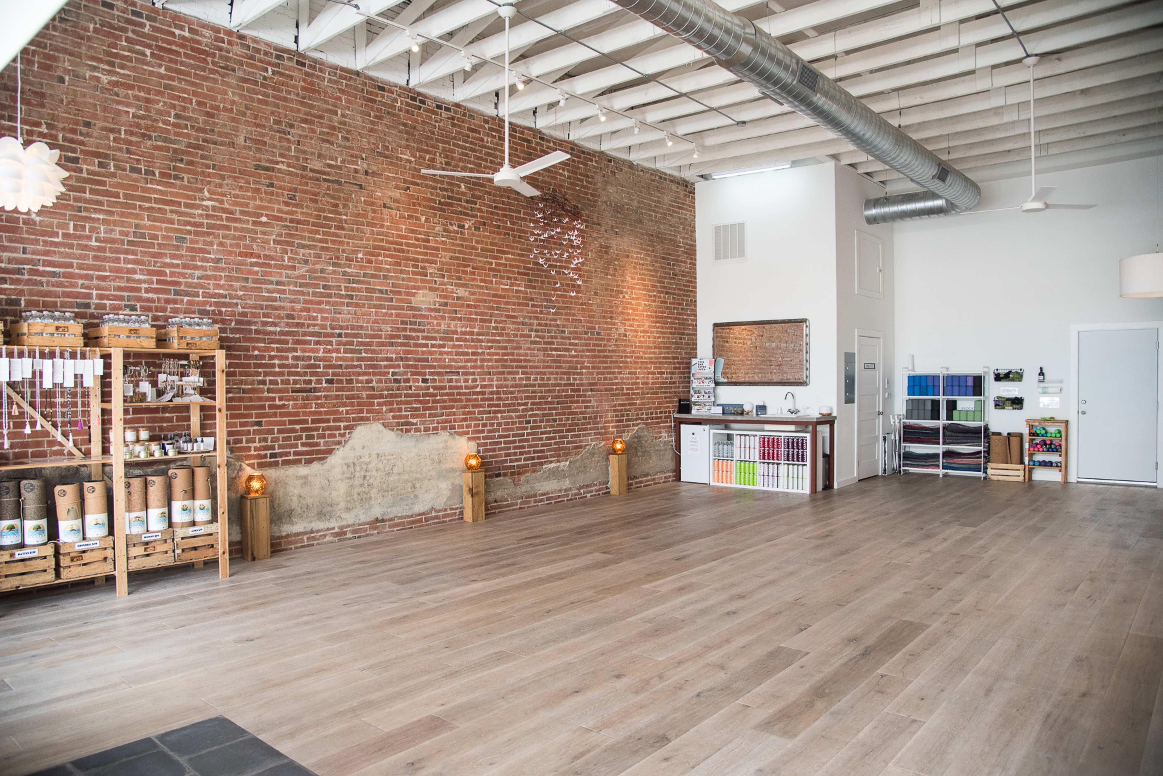 The interior of a spacious room features exposed brick walls, wooden flooring, and a well-organized area with shelving units along one side.