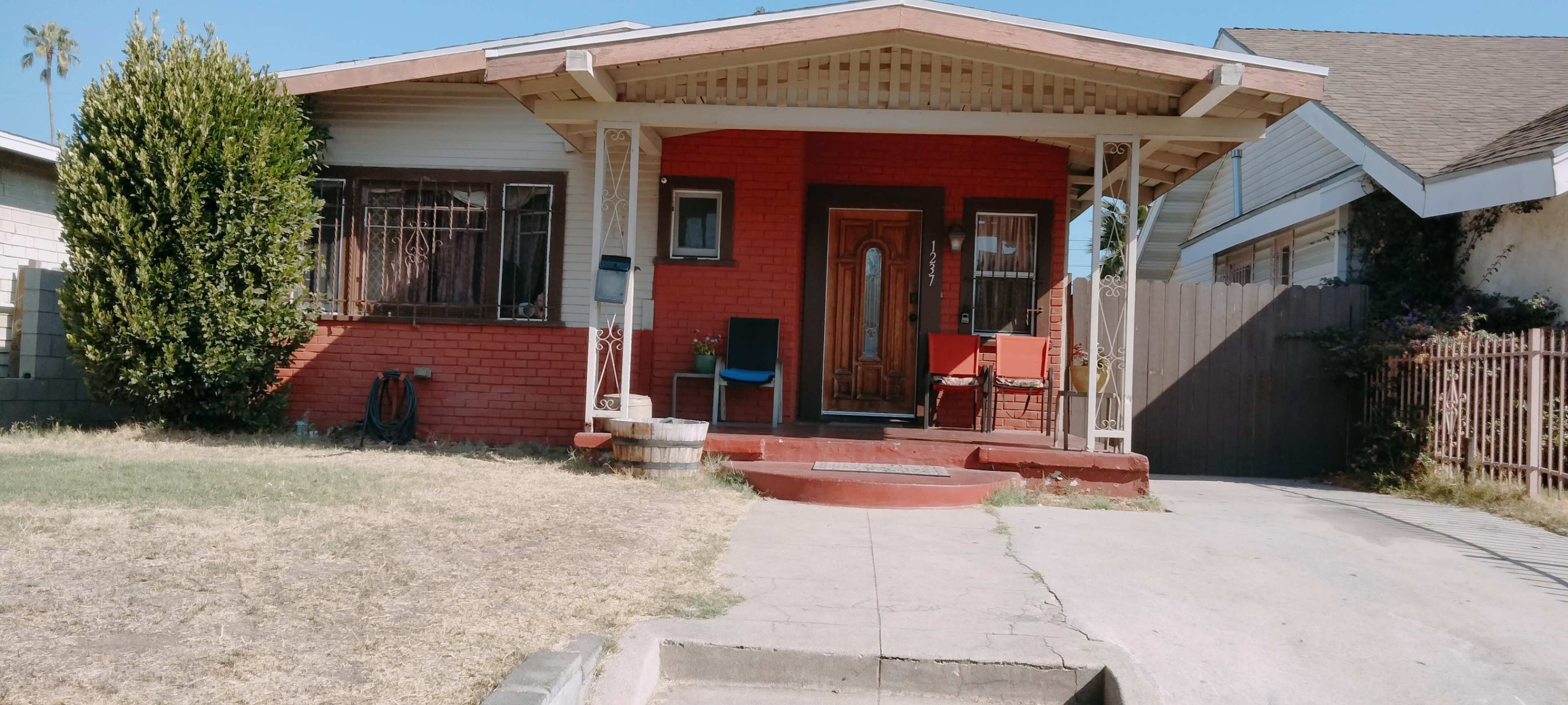 A single-story red brick house with a porch, a small front yard, and a paved walkway leading to the entrance.