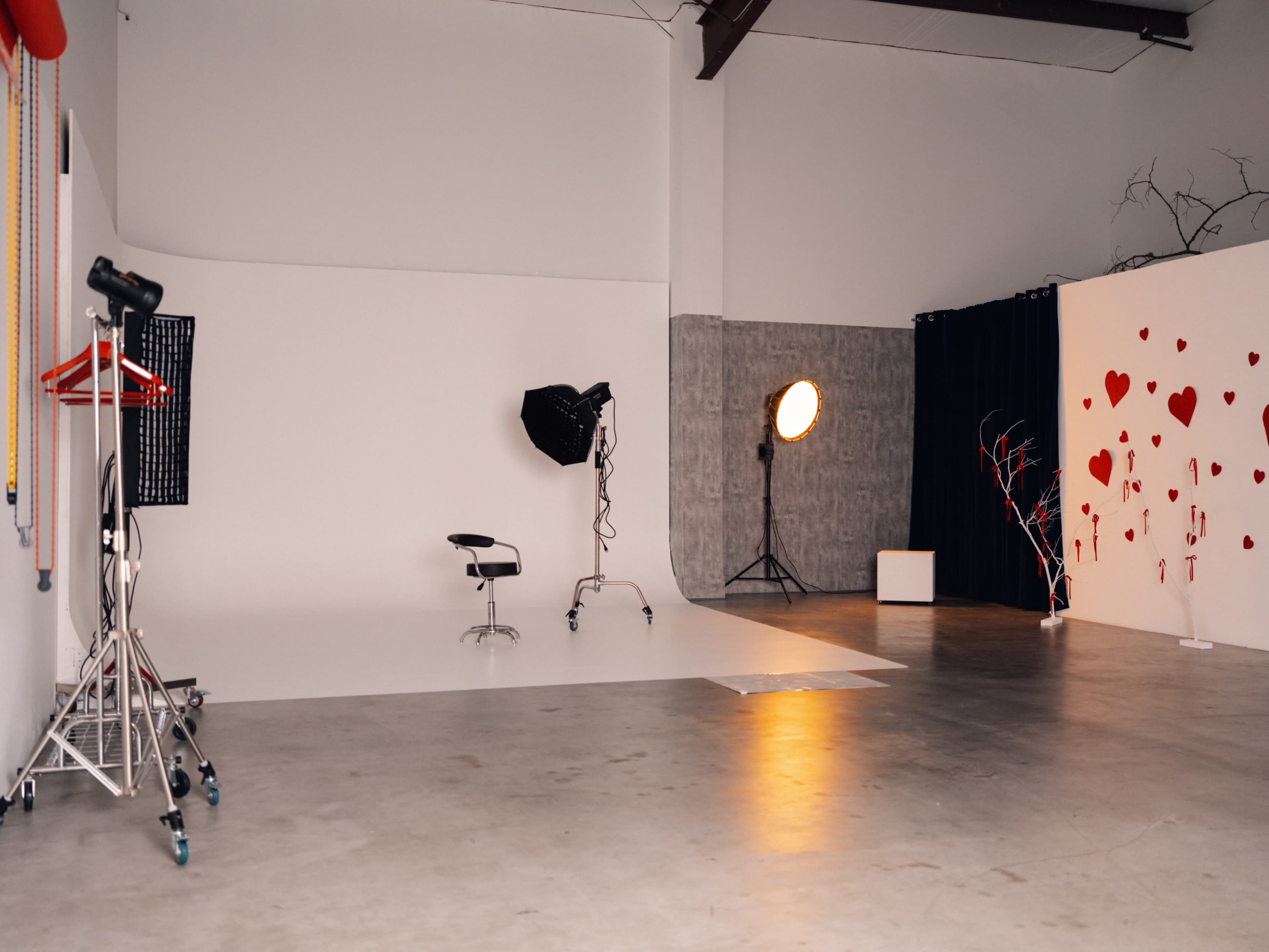 The image shows a photography studio with a white backdrop, a chair, and various lighting equipment set up around the room.