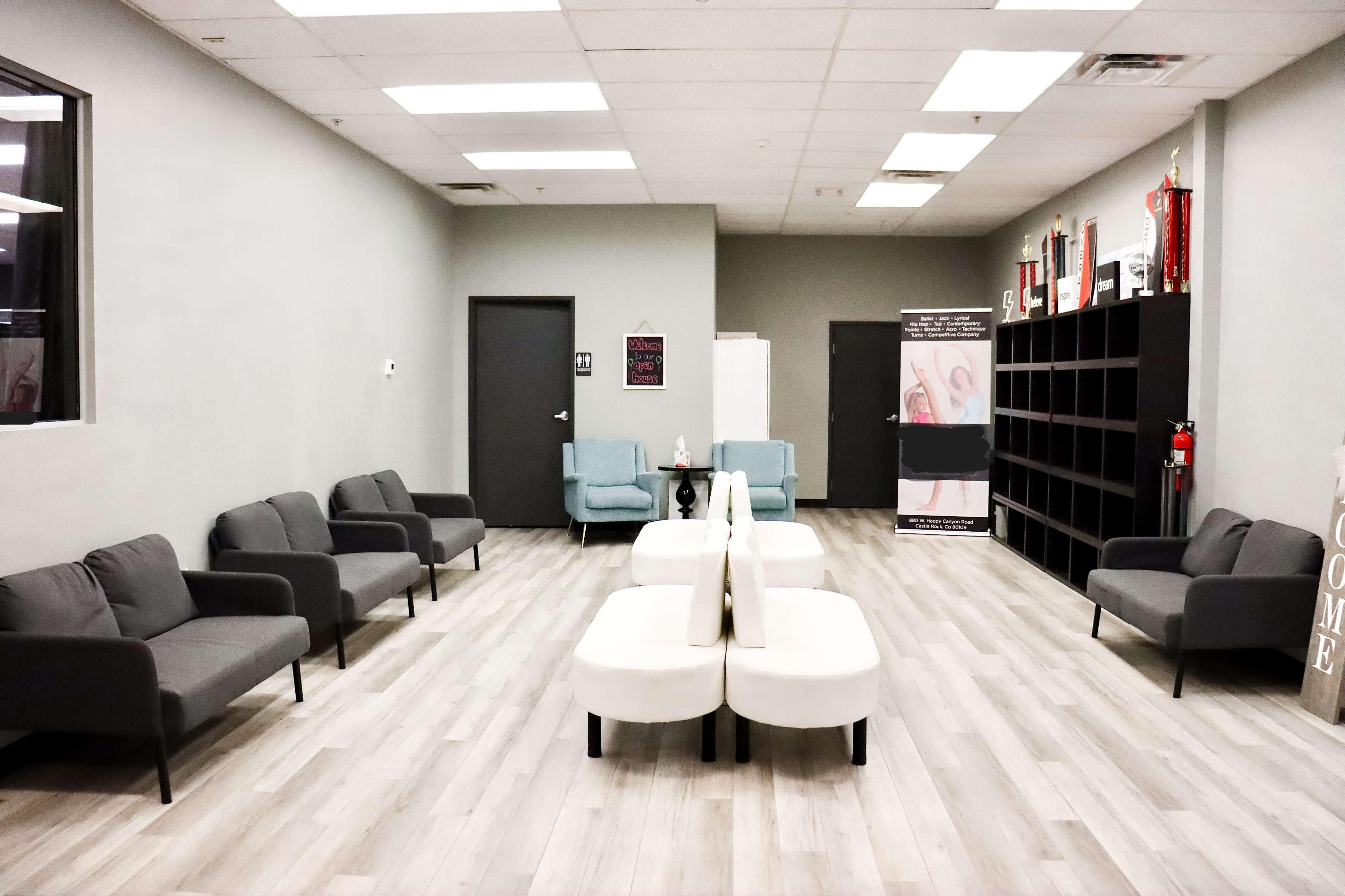 A waiting area with several gray couches and white tables, alongside a bookshelf and various decorations on the walls.
